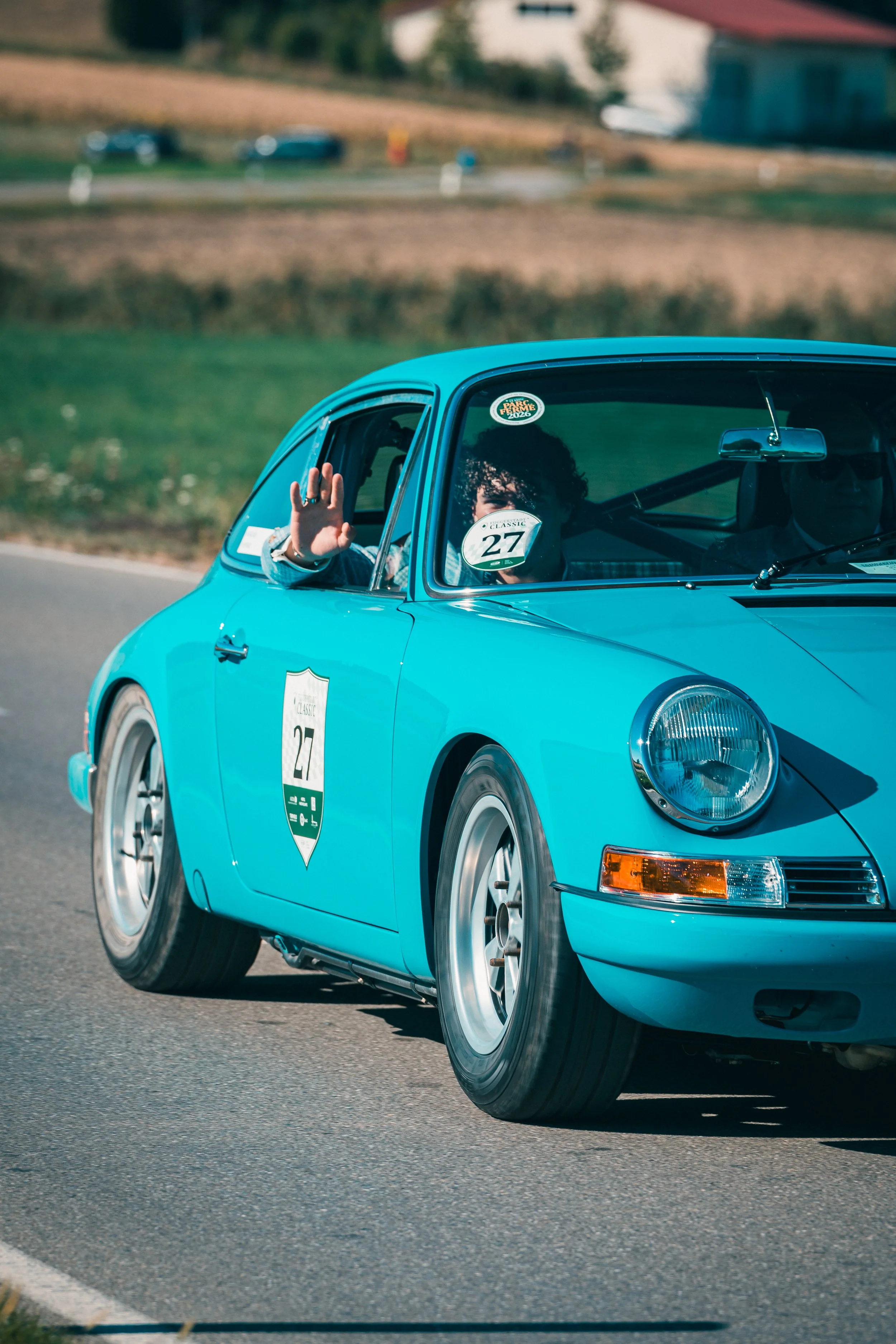 Hellblauer Porsche 911 mit Startnummer 27, Fahrer winkt aus dem Fenster