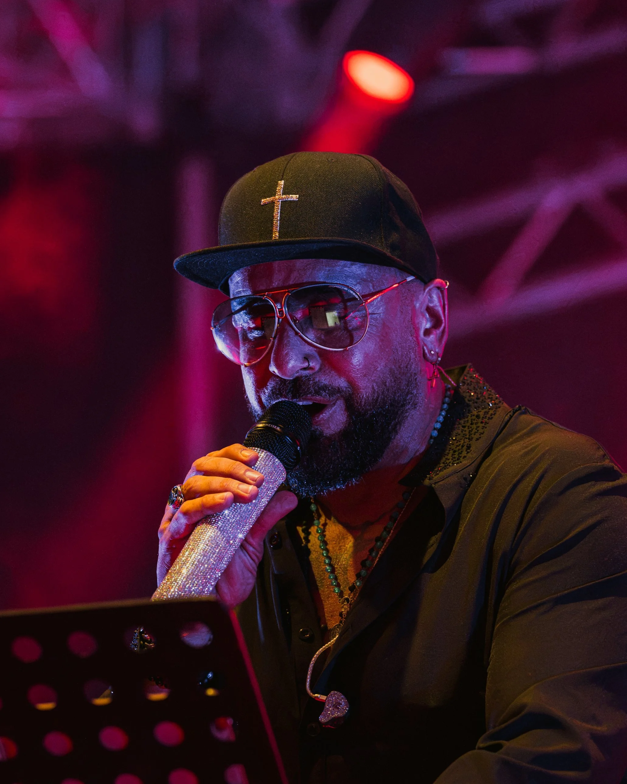 Domenico Salerno mit Kreuz-Cap und Glitzer-Mikrofon im Magenta-Licht – Konzertfotografie Kirchweih Gersthofen 2026