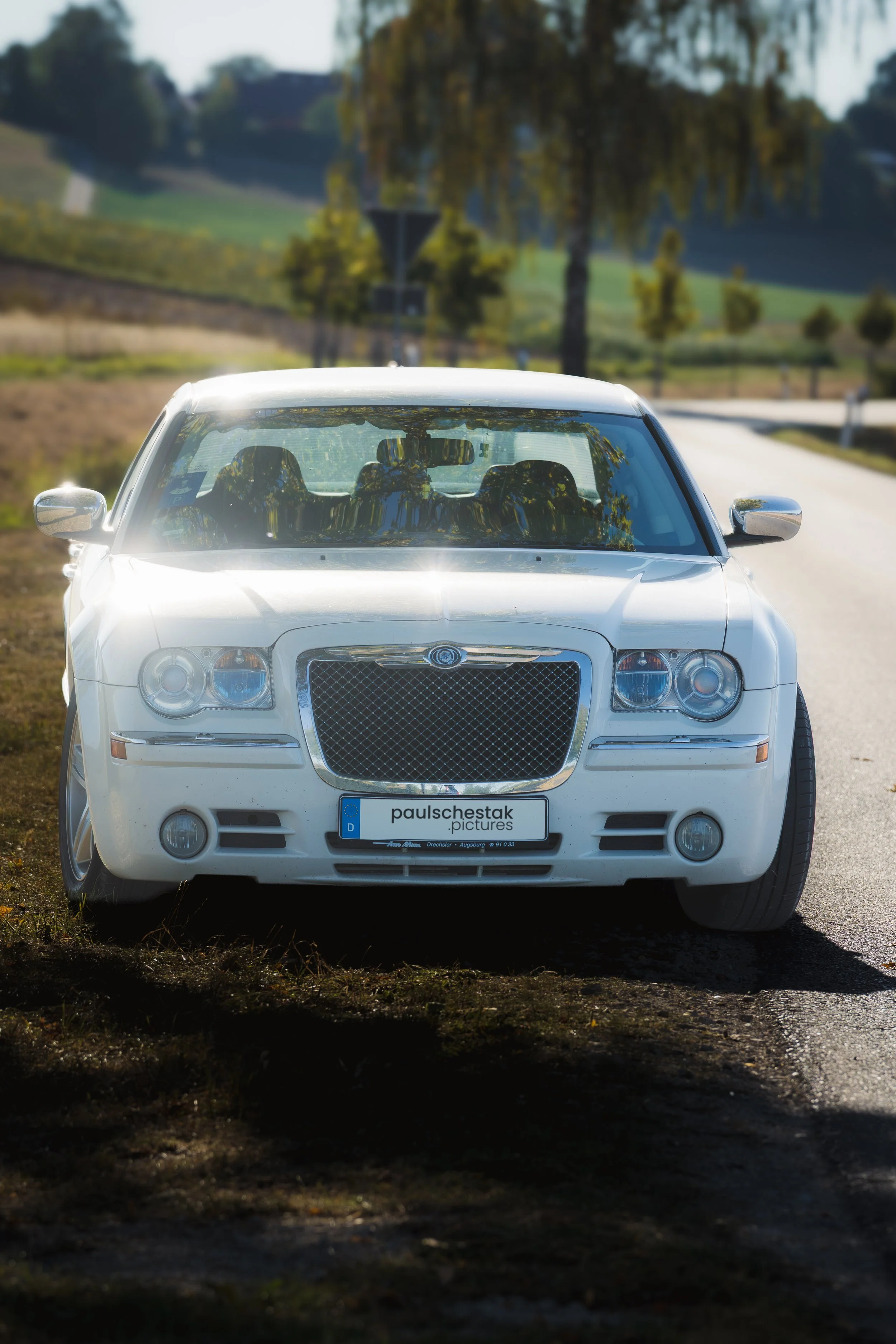 Weißer Chrysler 300C im Gegenlicht auf einer baumgesäumten Straße