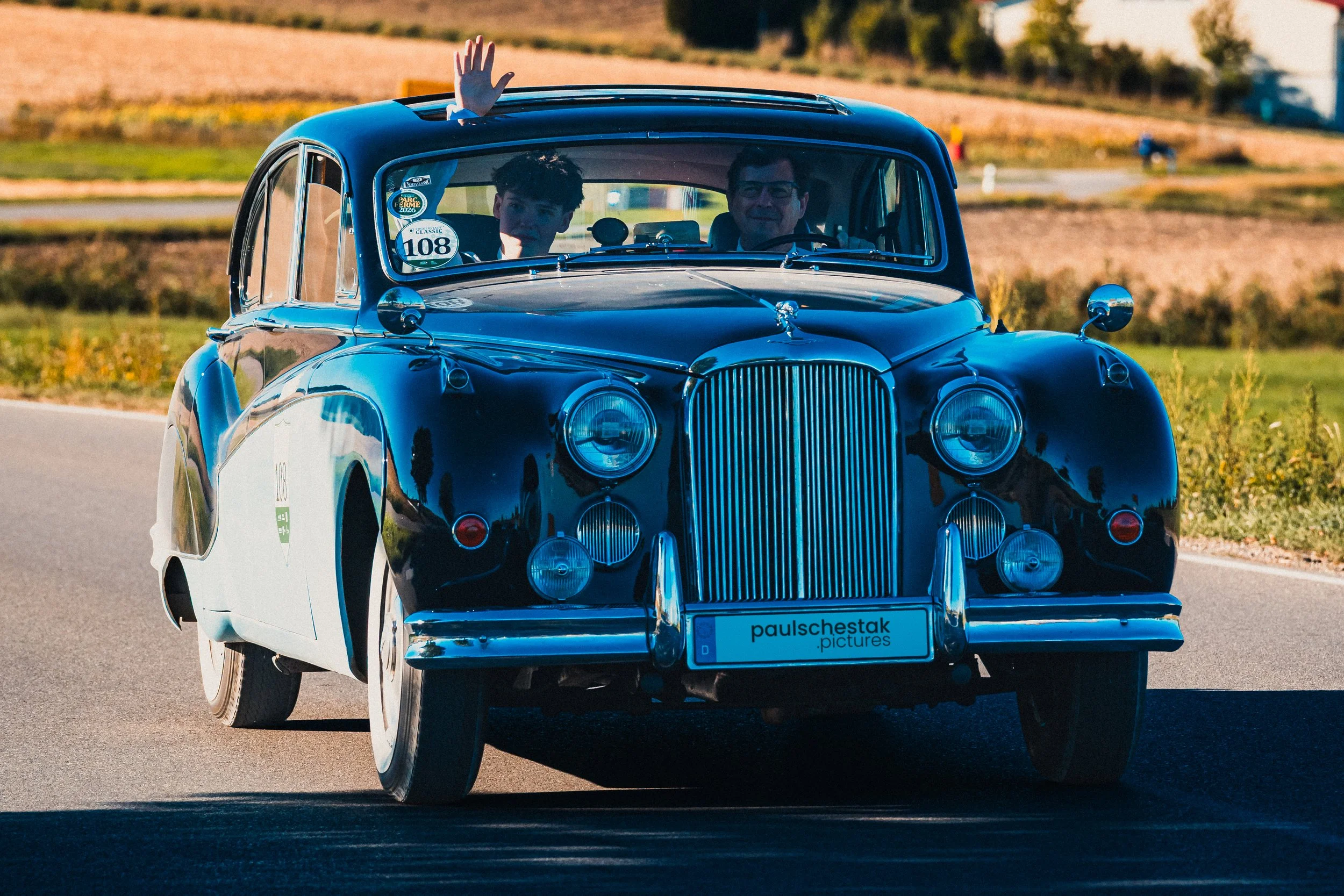 Dunkelblaue Oldtimer-Limousine mit Chromkühlergrill und winkendem Beifahrer