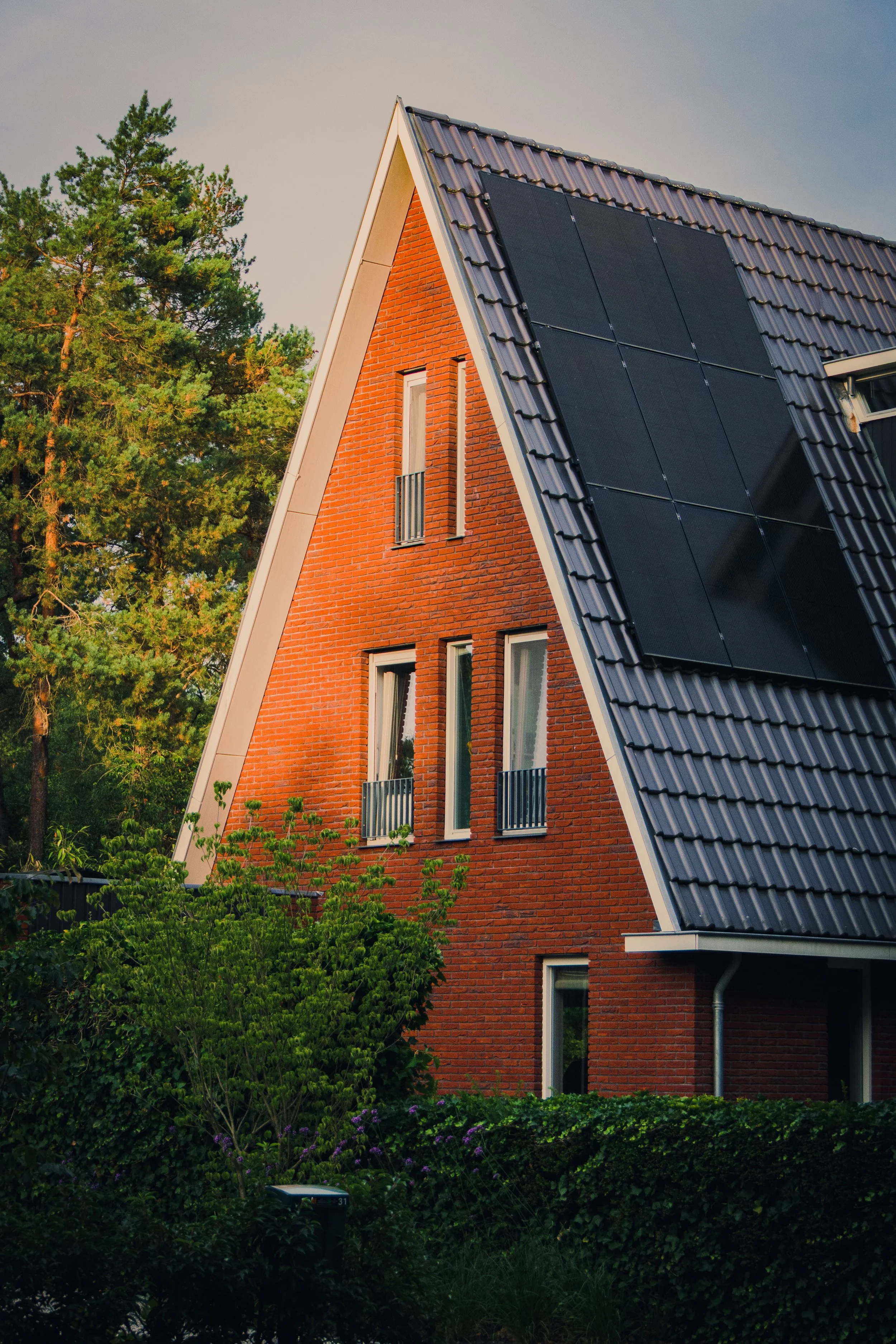 Giebelseite eines orangeroten Backsteinhauses mit Solarpanelen auf dem Dach, umgeben von Bäumen