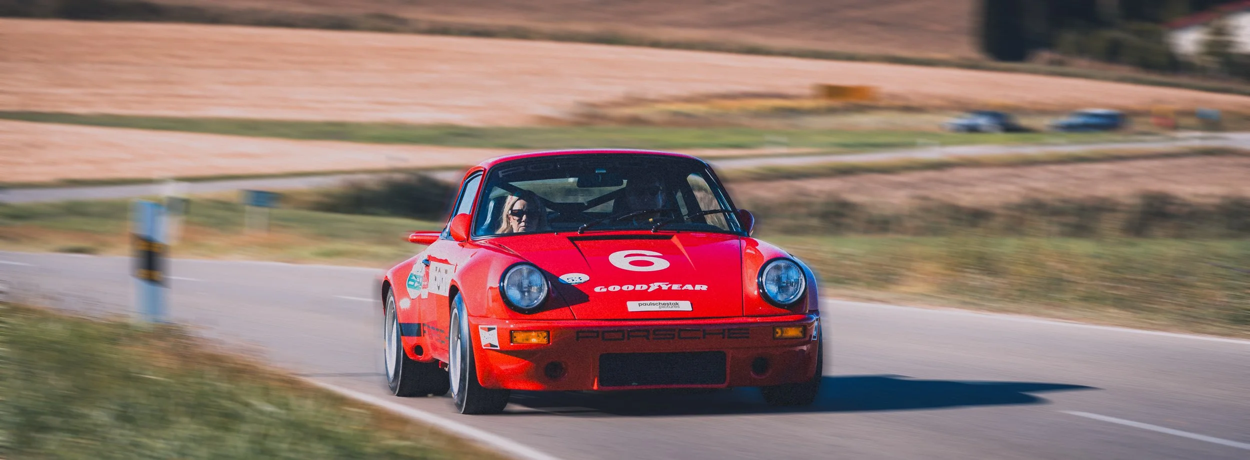 Roter Porsche 911 in Fahrt auf einer Landstraße zwischen Feldern