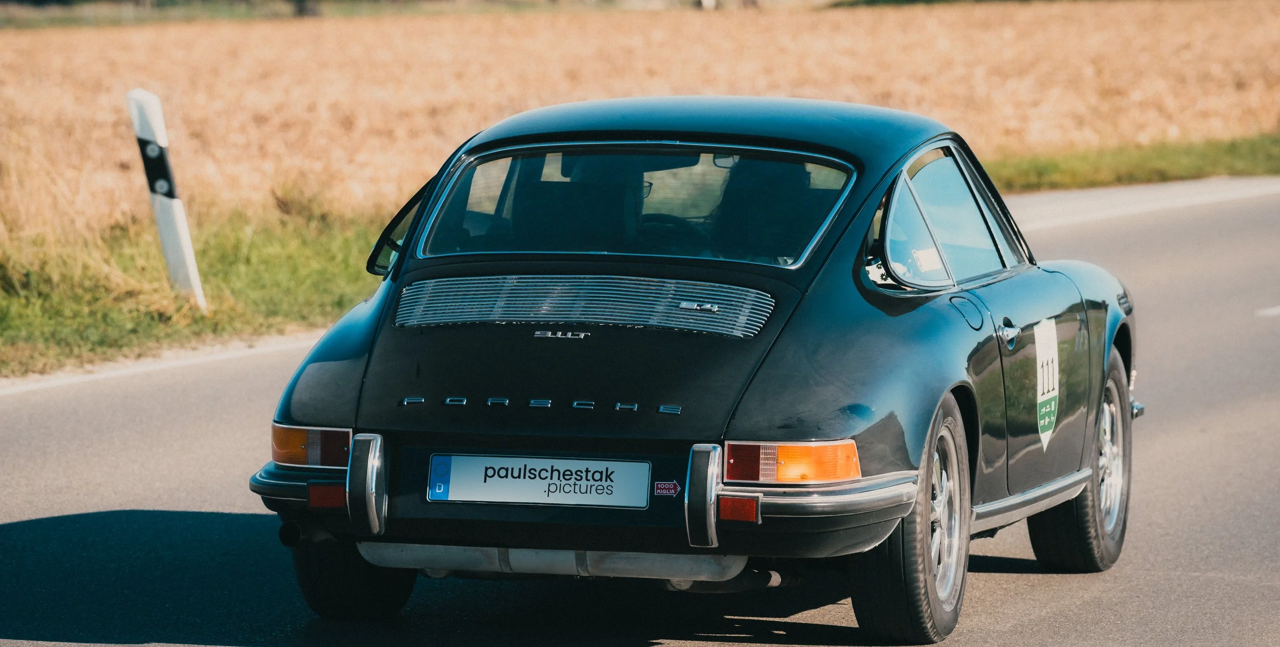 Dunkler klassischer Porsche 911 von hinten auf einer Landstraße