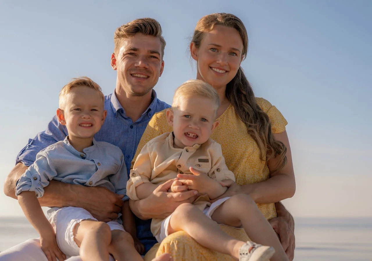 Familie am Strand, bestehend aus zwei Erwachsenen und zwei Kindern, gelbe und blaue Kleidung, sonniger Tag, blaue Himmel