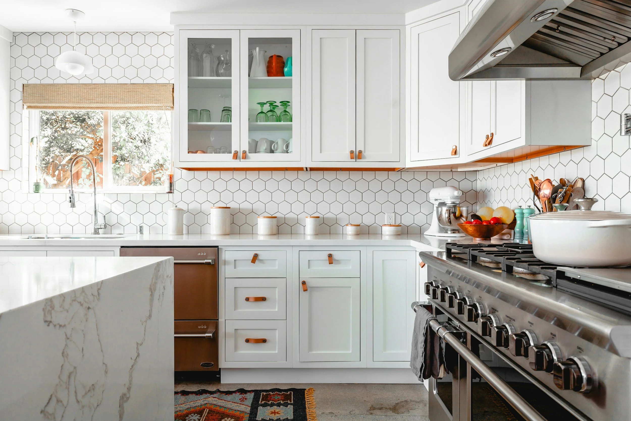 Modern kitchen with white cabinets, hexagon tile backsplash, stainless steel stove, and window with natural light.