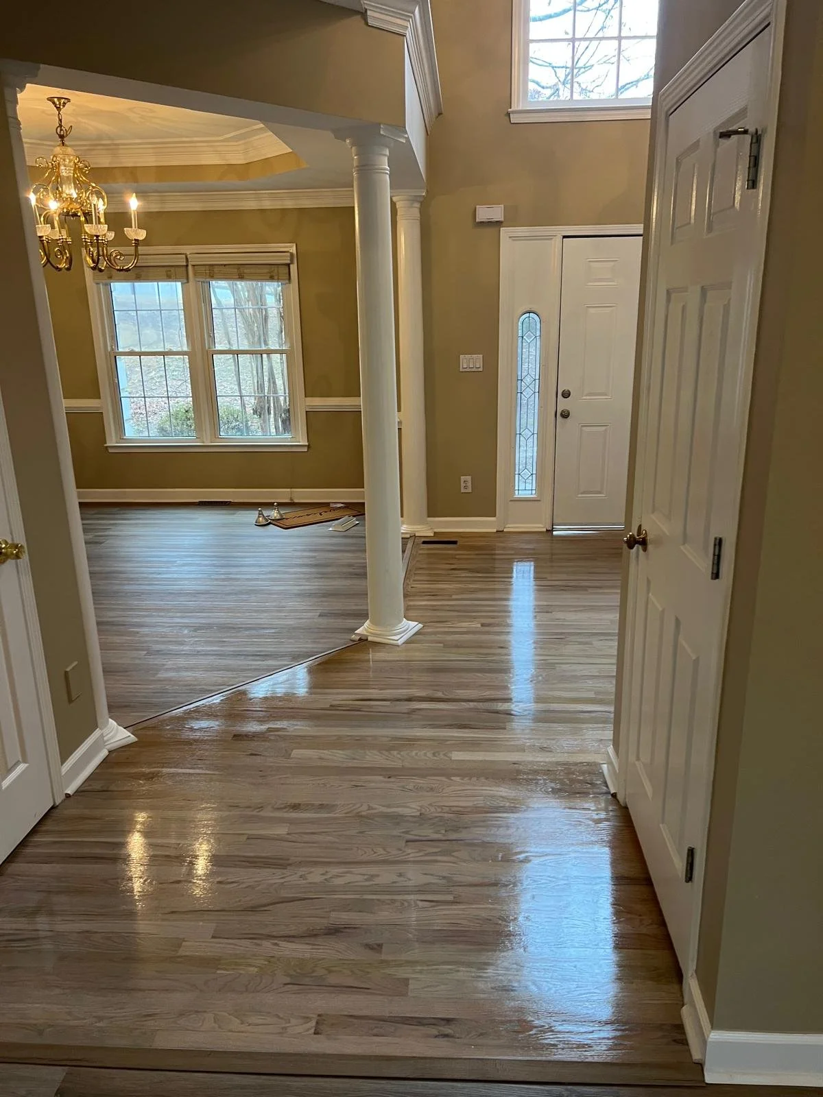 View of a home's entryway with hardwood floors, white trim, a front door with glass, a window, and part of a chandelier visible.