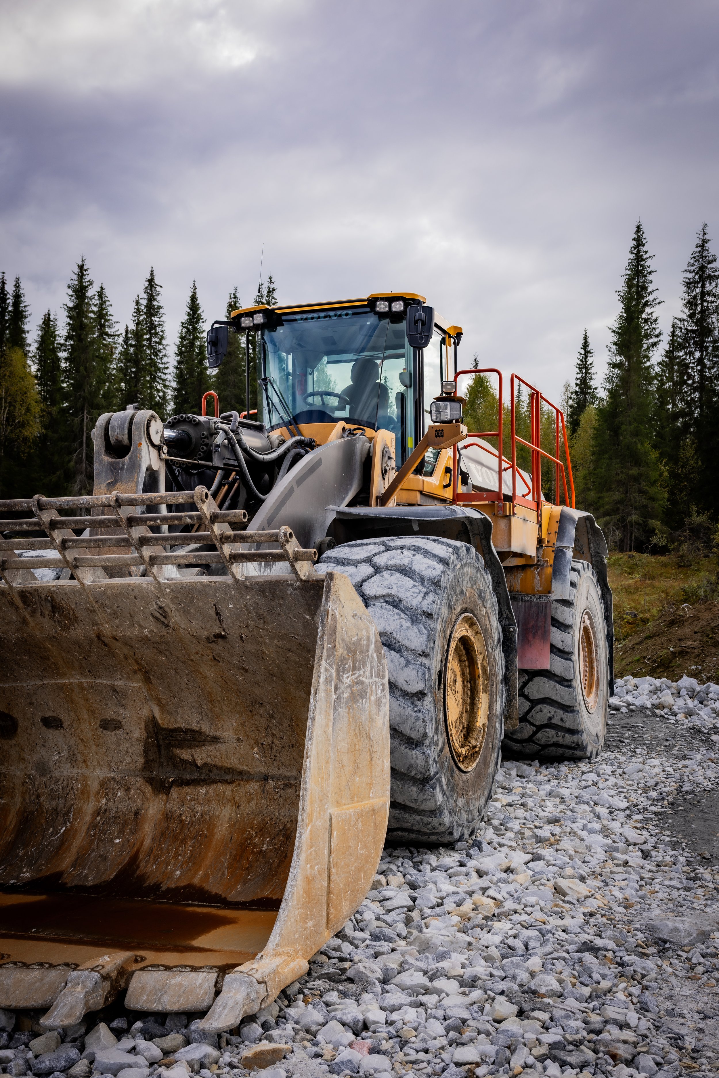 A large yellow and black tractor parked outdoors on muddy ground under a cloudy sky.