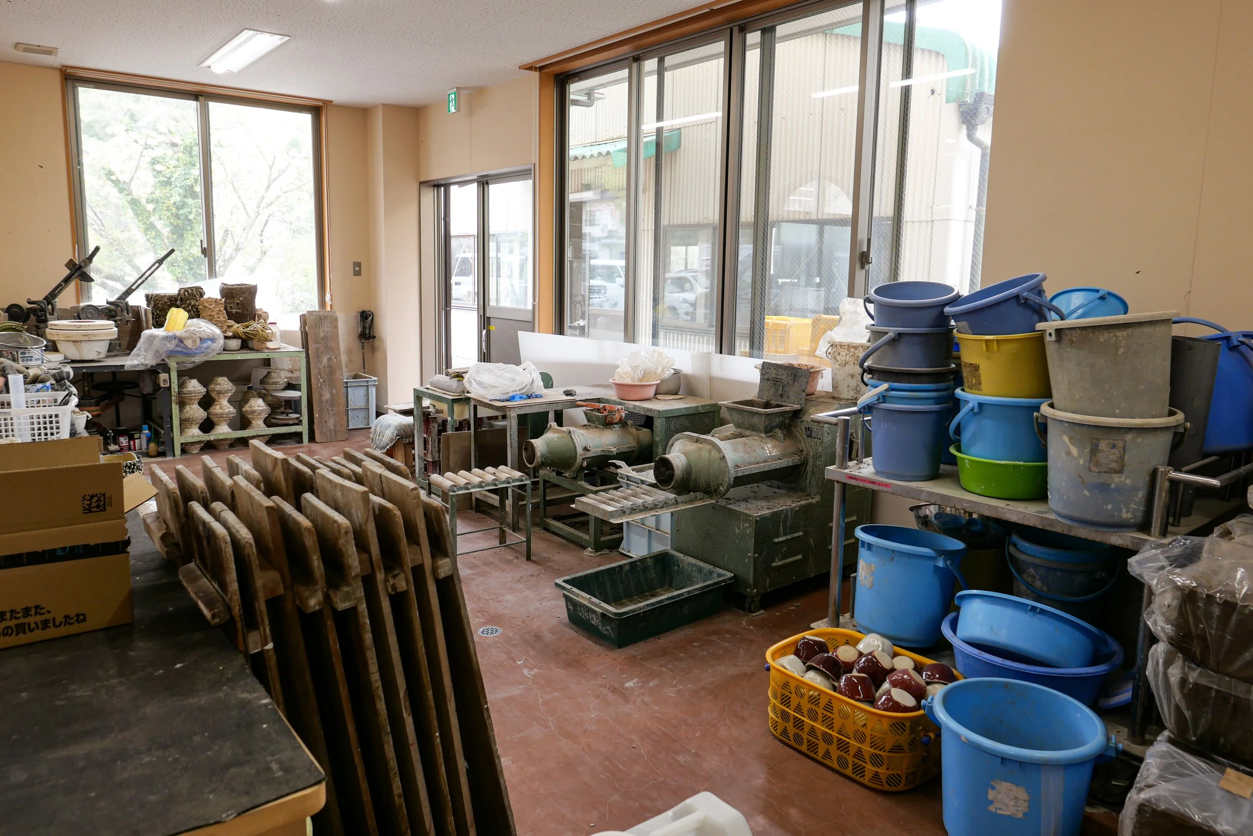 the back room of the shigaraki seinenryo workshop, filled with clay-processing machinery, wooden drying boards, and stacks of buckets.