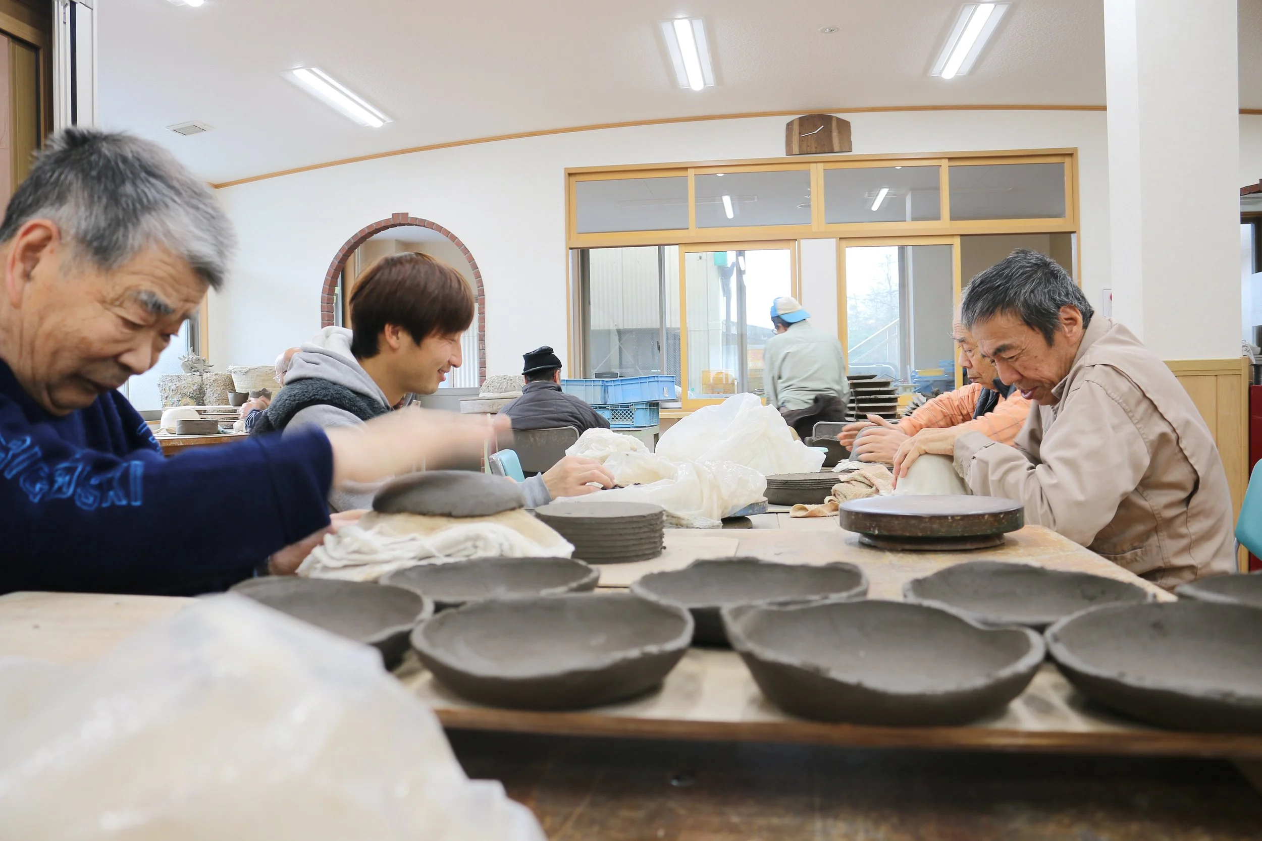 shigaraki potters working side by side at a large table in the shigaraki seinenryo workshop, shaping unfired clay plates and bowls by hand.