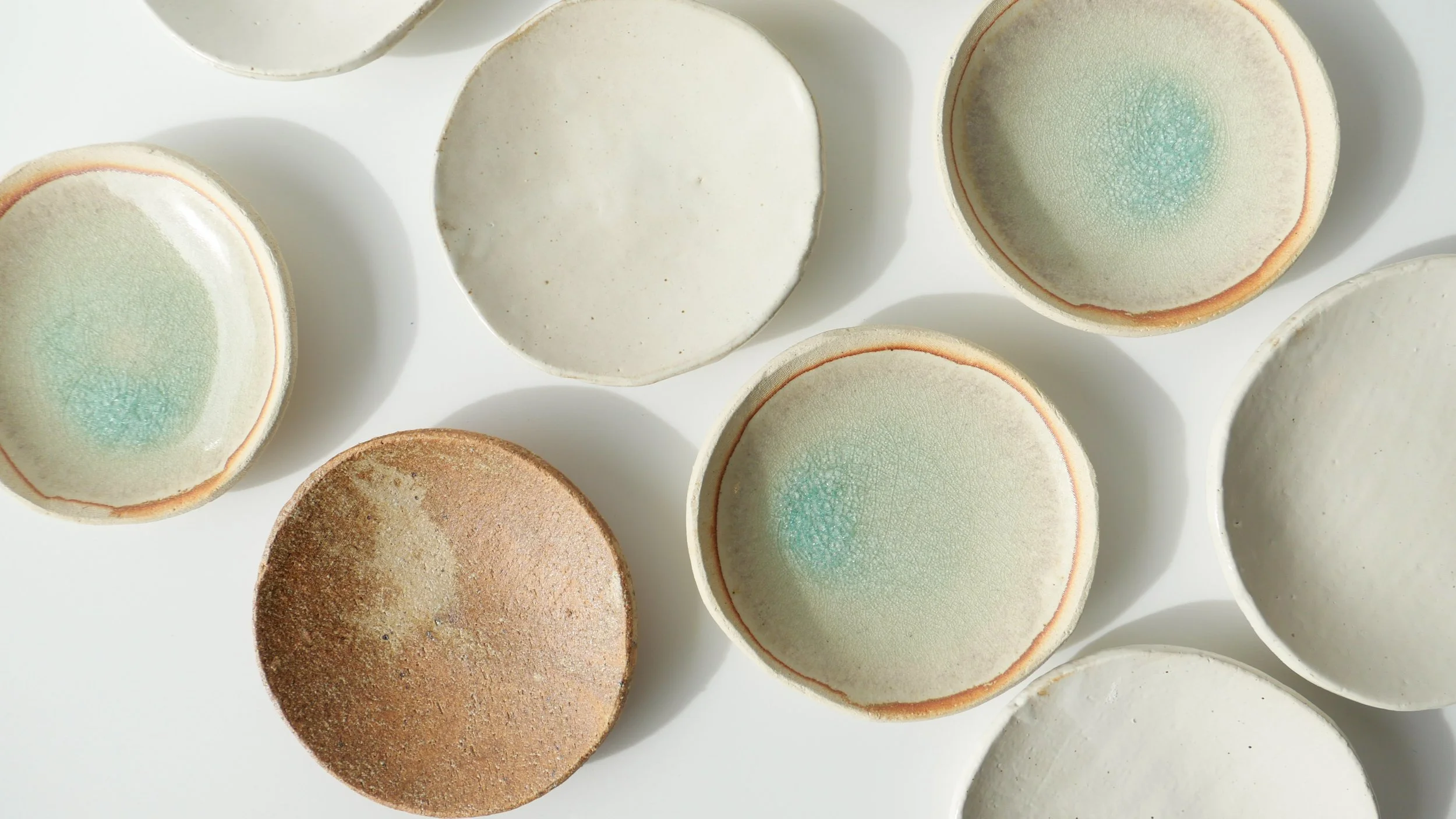 A collection of circular ceramic dishes with varying pastel colors and textures, arranged on a white surface.