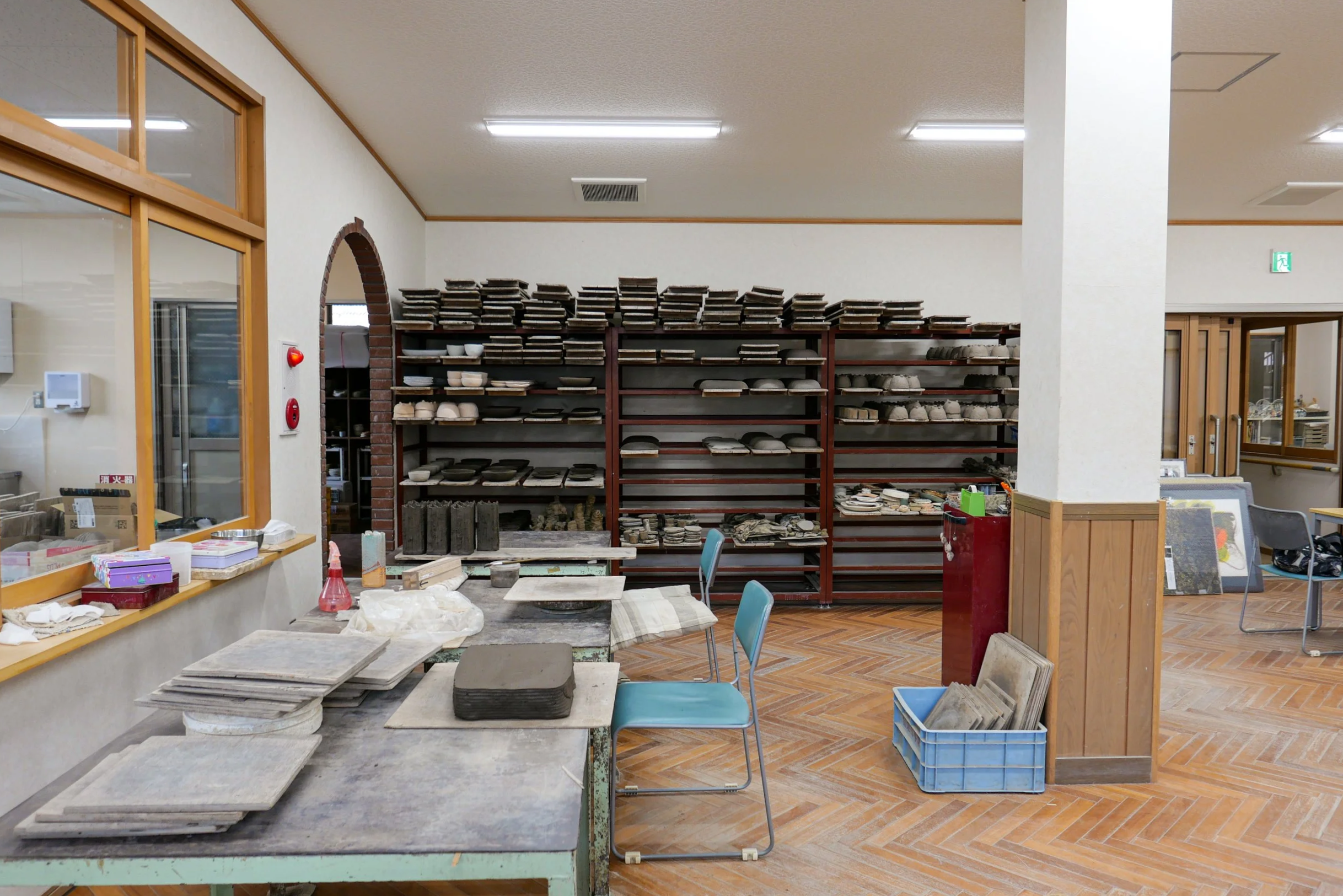 the interior of shigaraki seinenryo workshop, with shelves of unfired clay pieces drying on racks along the wall and work tables in the foreground covered with clay slabs and moulds.