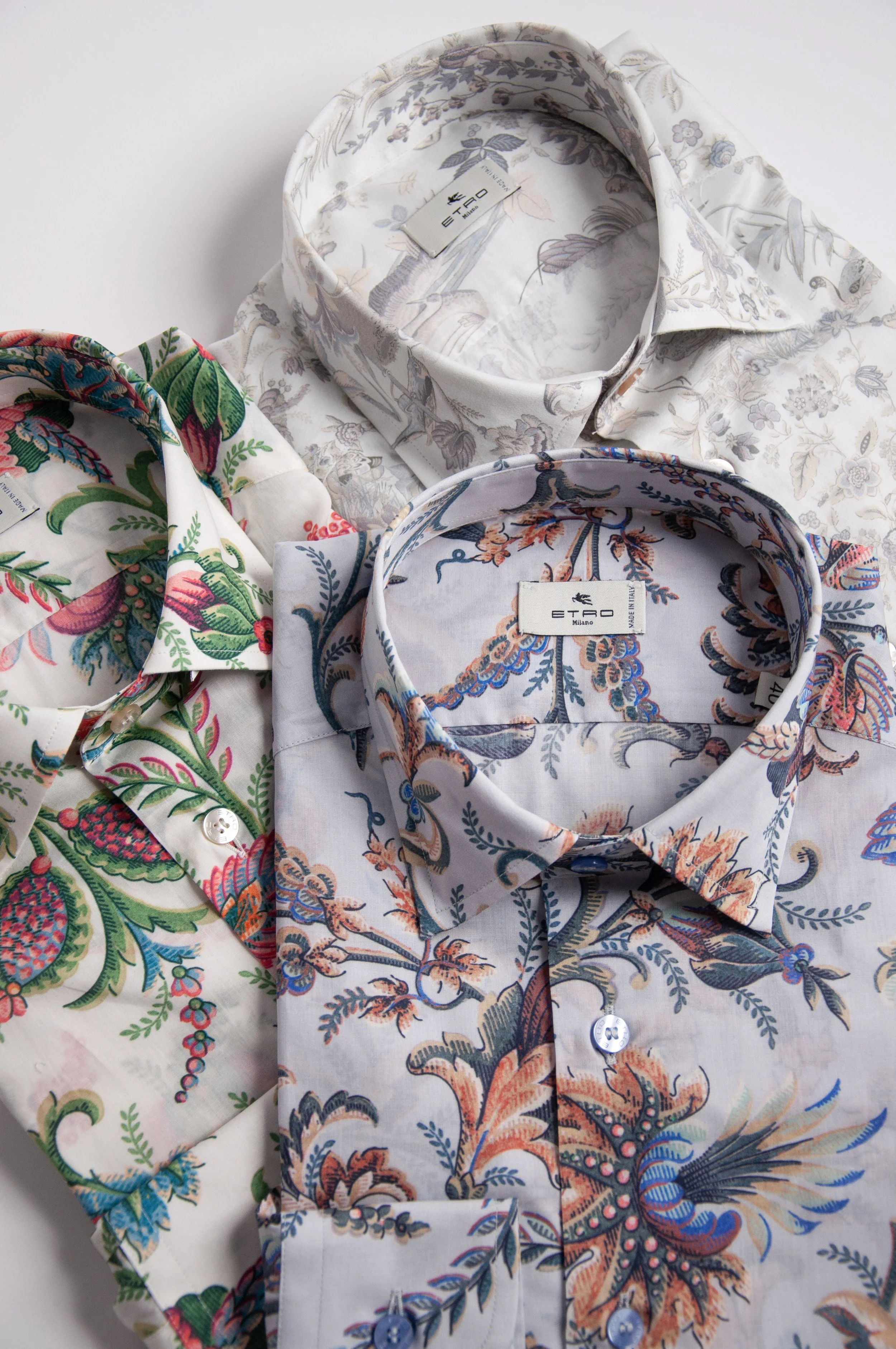 Three long-sleeve button-up shirts with floral patterns, laid out flat on a white surface. The shirts have intricate, colorful botanical designs on a light background.