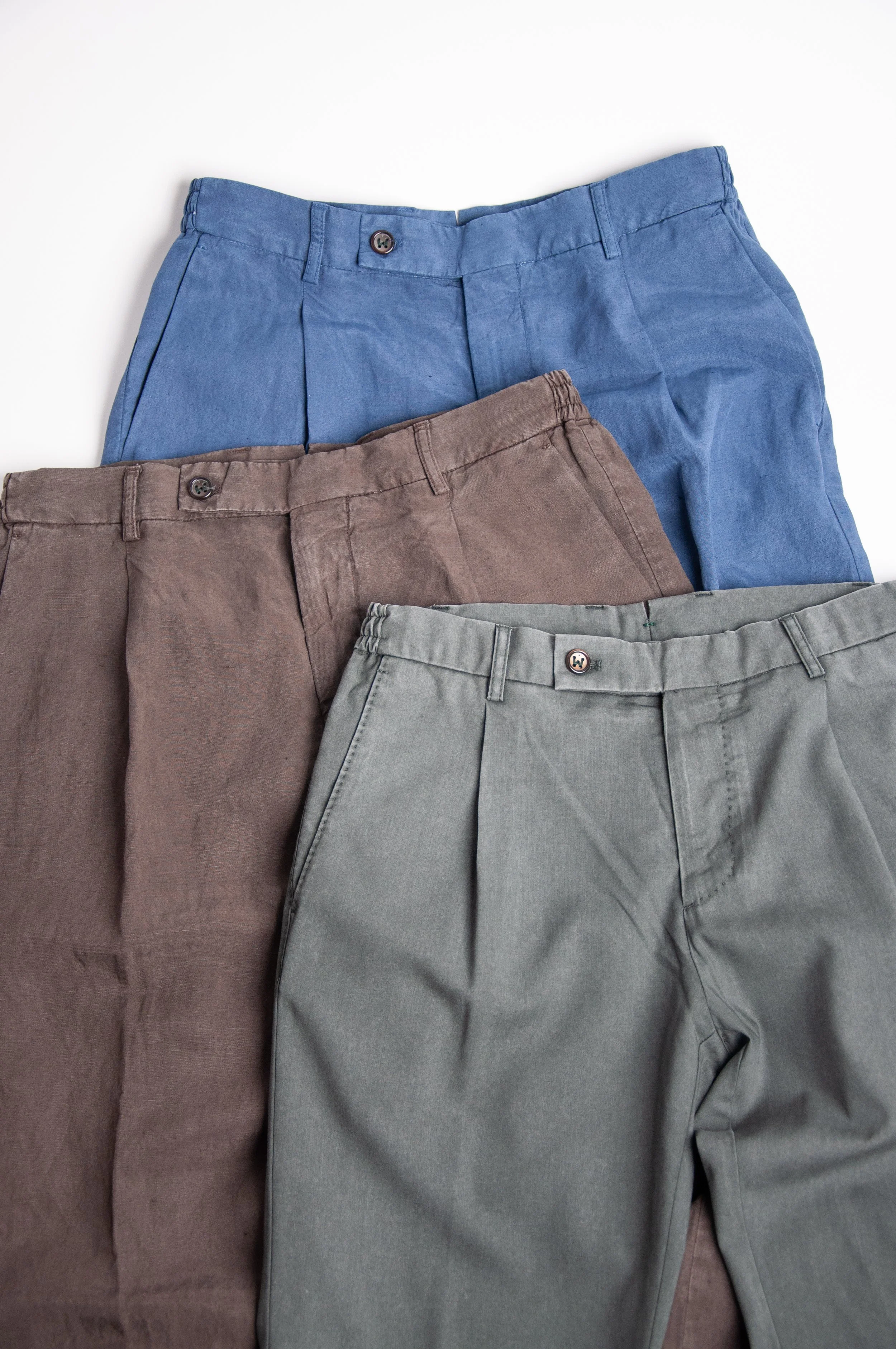 Three pairs of men's pants in blue, brown, and gray laid flat on a white surface.
