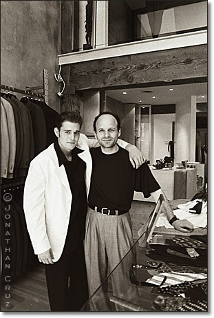 Two men standing side by side in a clothing store with shelves of clothes in the background.