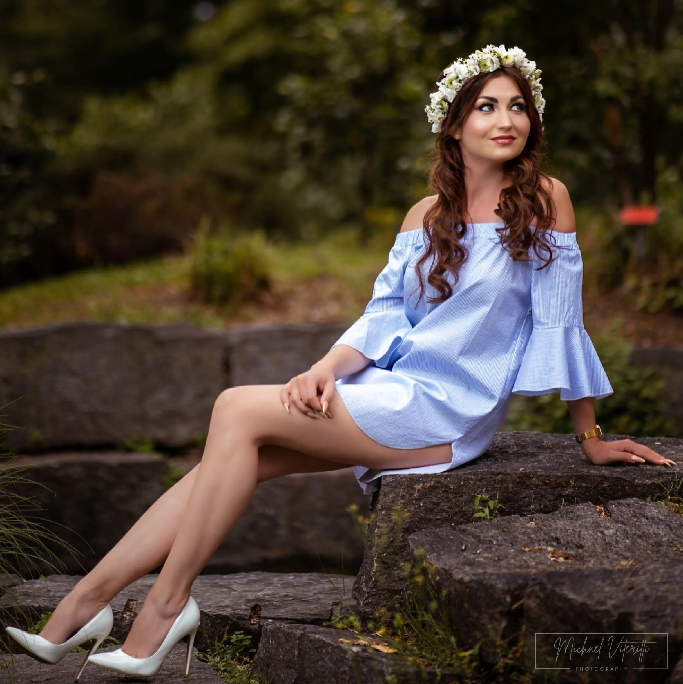 Donna con corona di fiori seduta su un tronco in un ambiente naturale