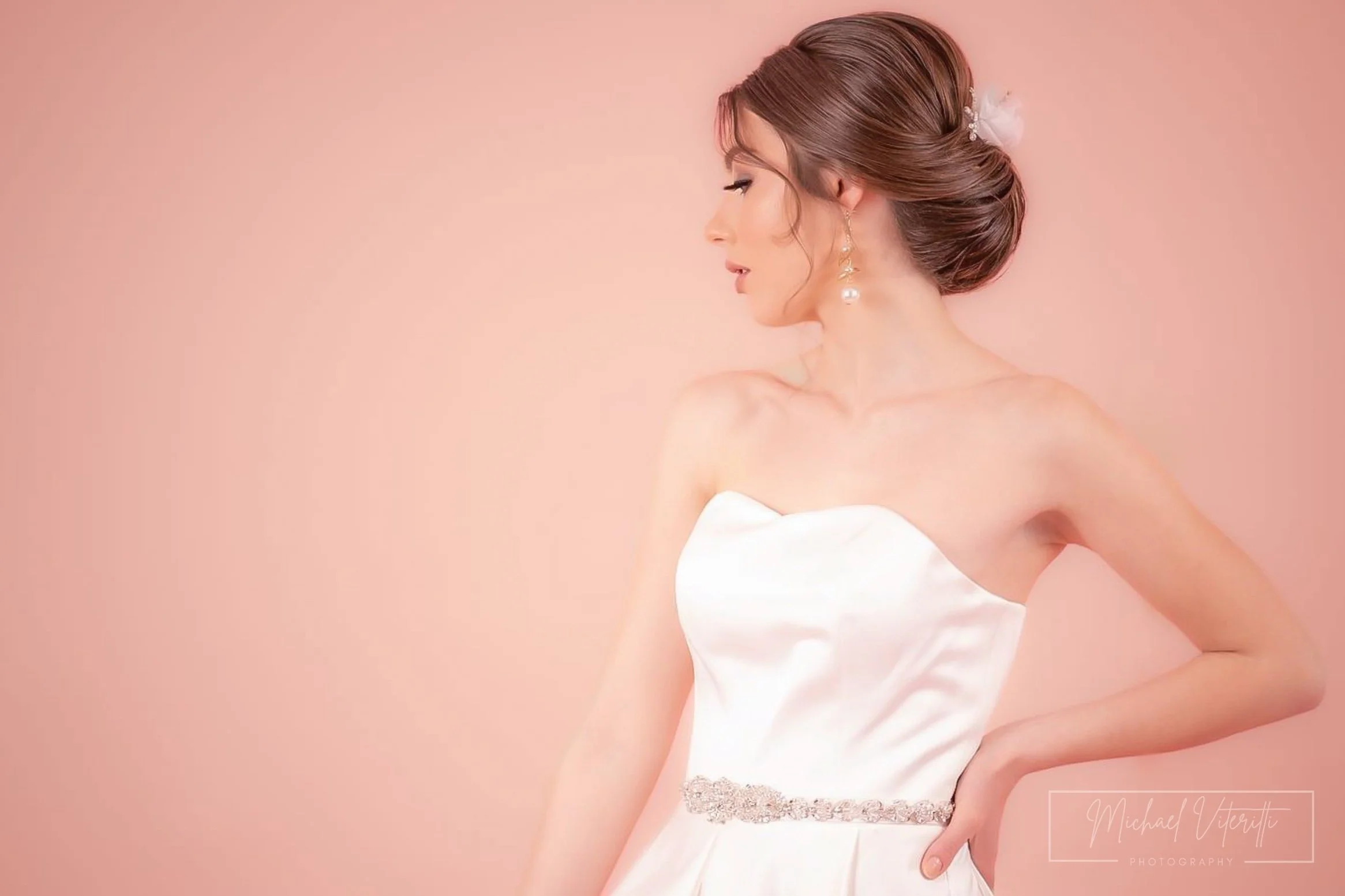 Ritratto di una donna con acconciatura elegante, orecchini pendenti e abito bianco, sulla destra di uno sfondo rosa