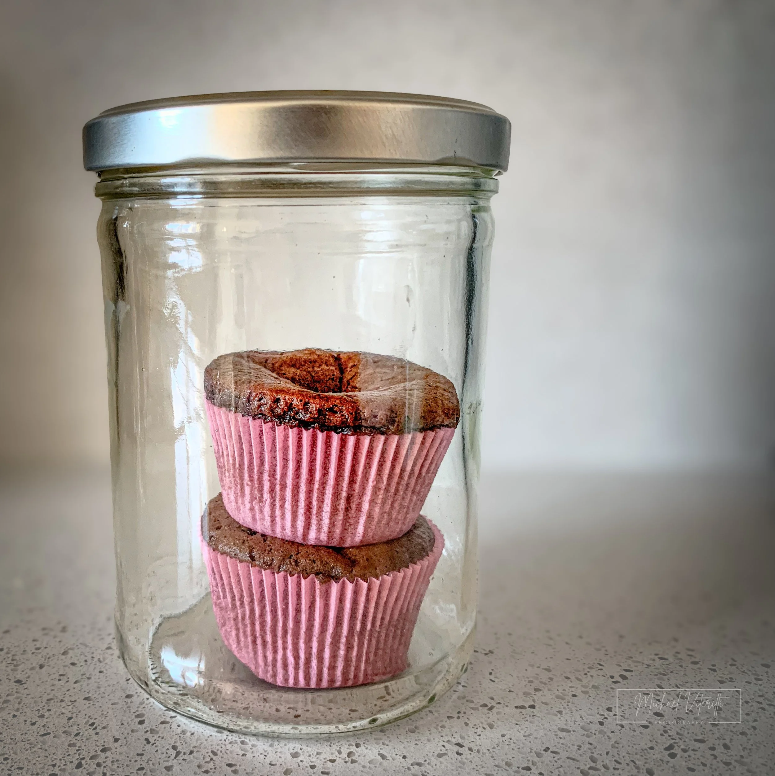 Barattolo di vetro con una muffin al cioccolato dentro, appoggiato su un tavolo di granito.