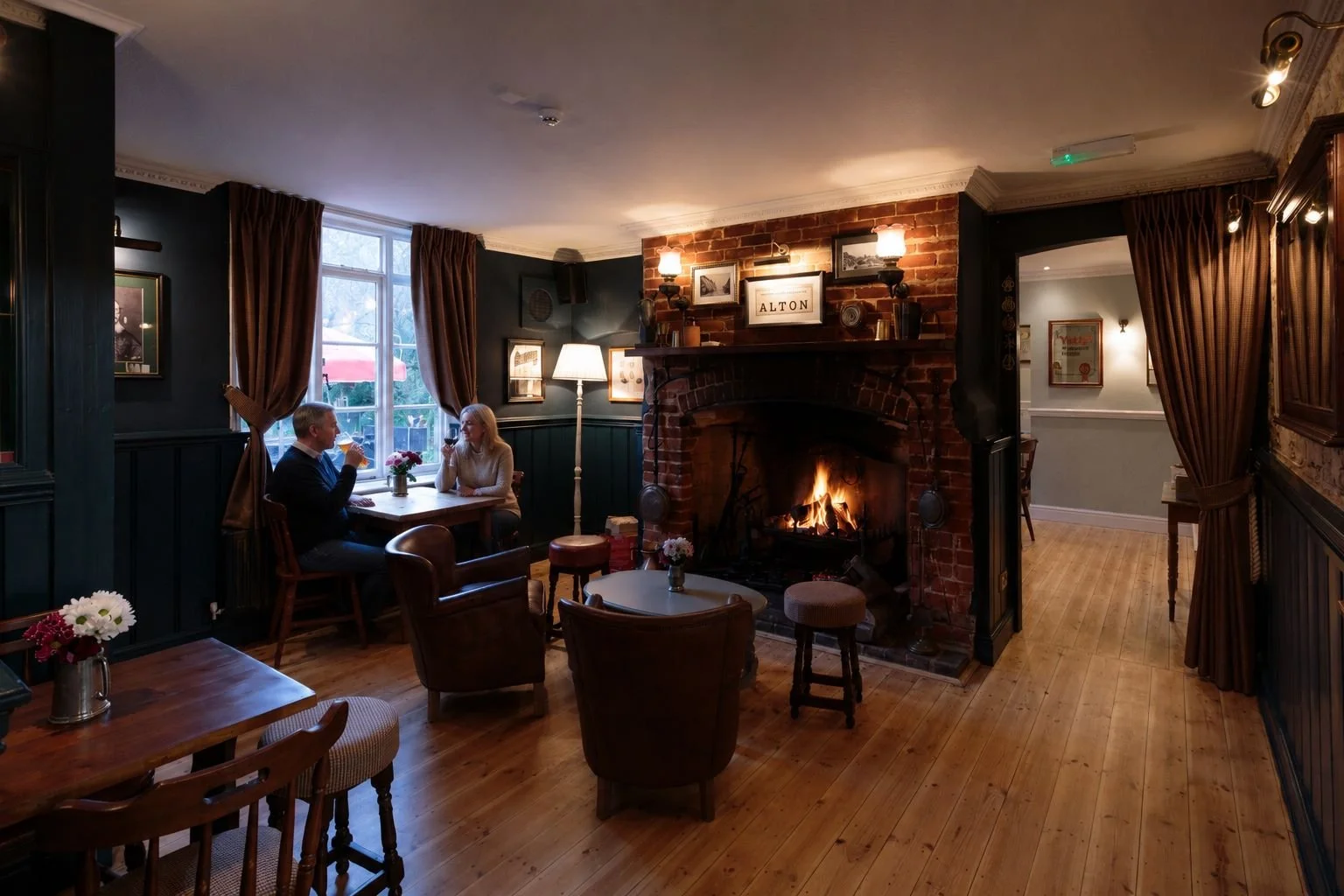 Cozy restaurant with a fireplace, couple drinking red wine, dark wood furniture, framed pictures, large window with curtains, and warm ambient lighting.