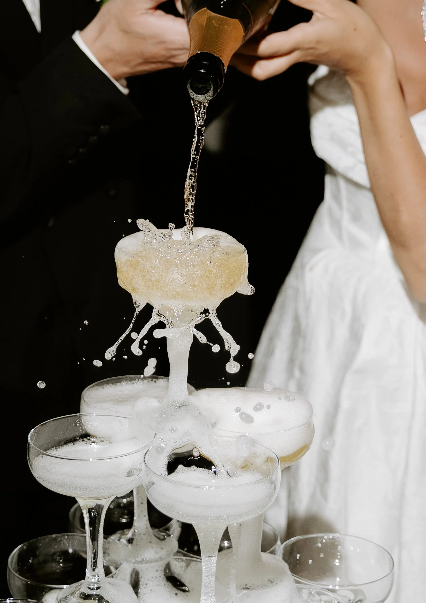 Ein Champagnerkühler mit mehreren leeren Sektgläsern, in die Champagner eingeschenkt wird, bei einer Feier oder Hochzeit.