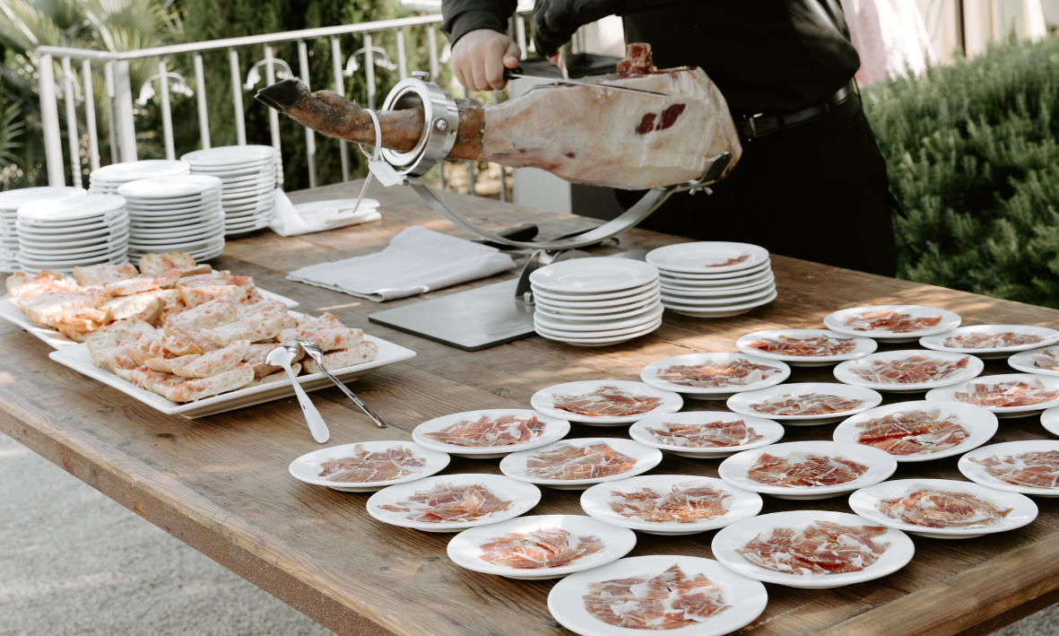 Person bereitet herzhaften spanischen Schinken (Jamón) auf einem Tisch mit weißen Tellern vor.