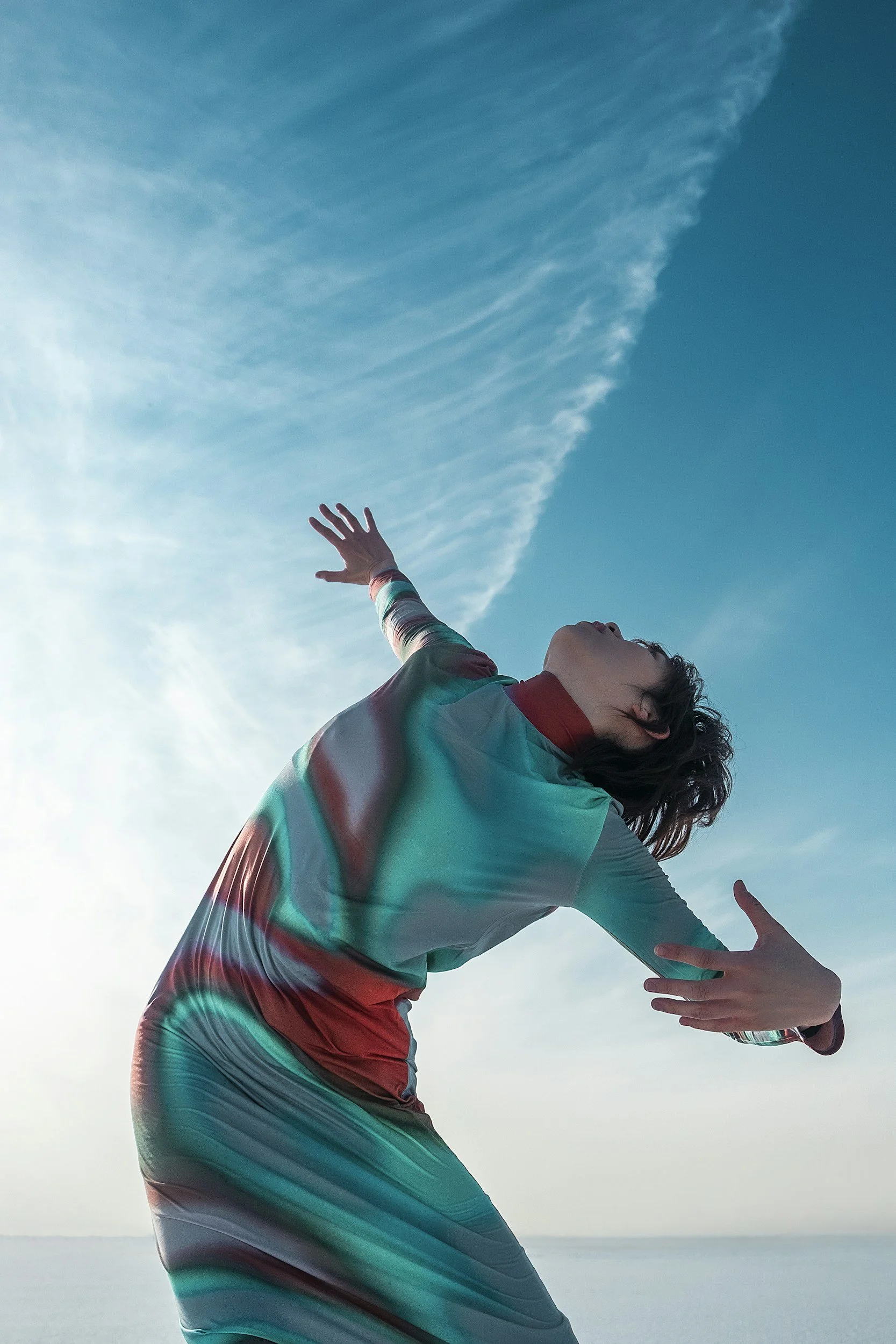 Person with curly hair wearing a colorful, striped jacket reaching upward against a blue sky with wispy clouds.  The picture depicts that JWB Research will help a brand grow and organisation get the research they need to move forward