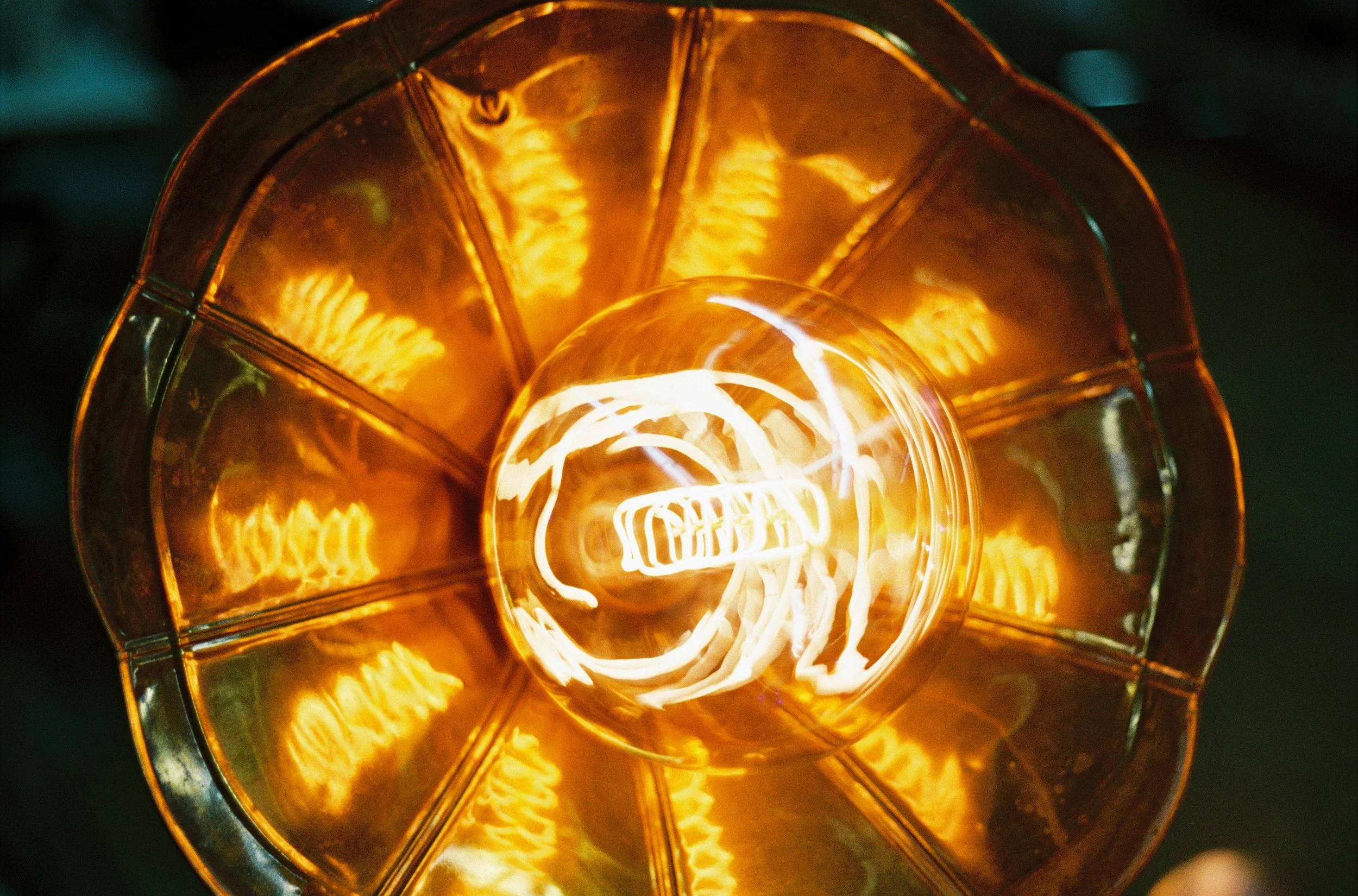 Nahaufnahme einer Glühbirne mit sichtbarer glühender Wolframspirale und orangefarbenem Glühfaden, eingeklemmt in einem Glasgehäuse