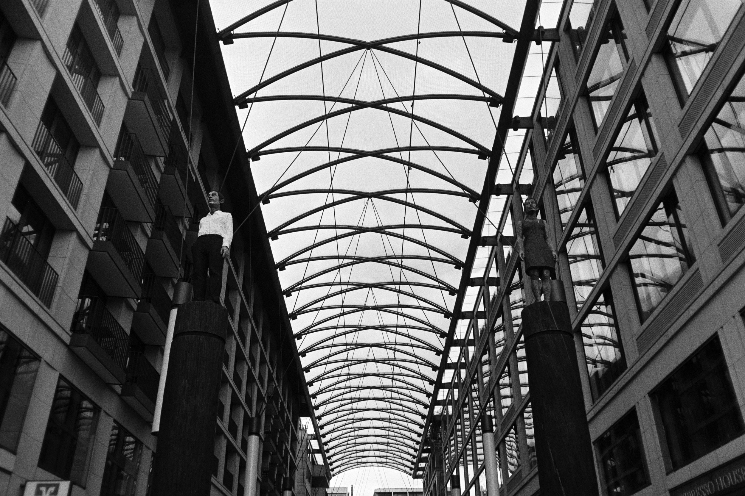 Schwarzweißfoto eines modernen Innenhofs mit Glas- und Stahlarchitektur und zwei Skulpturen an den Säulen
