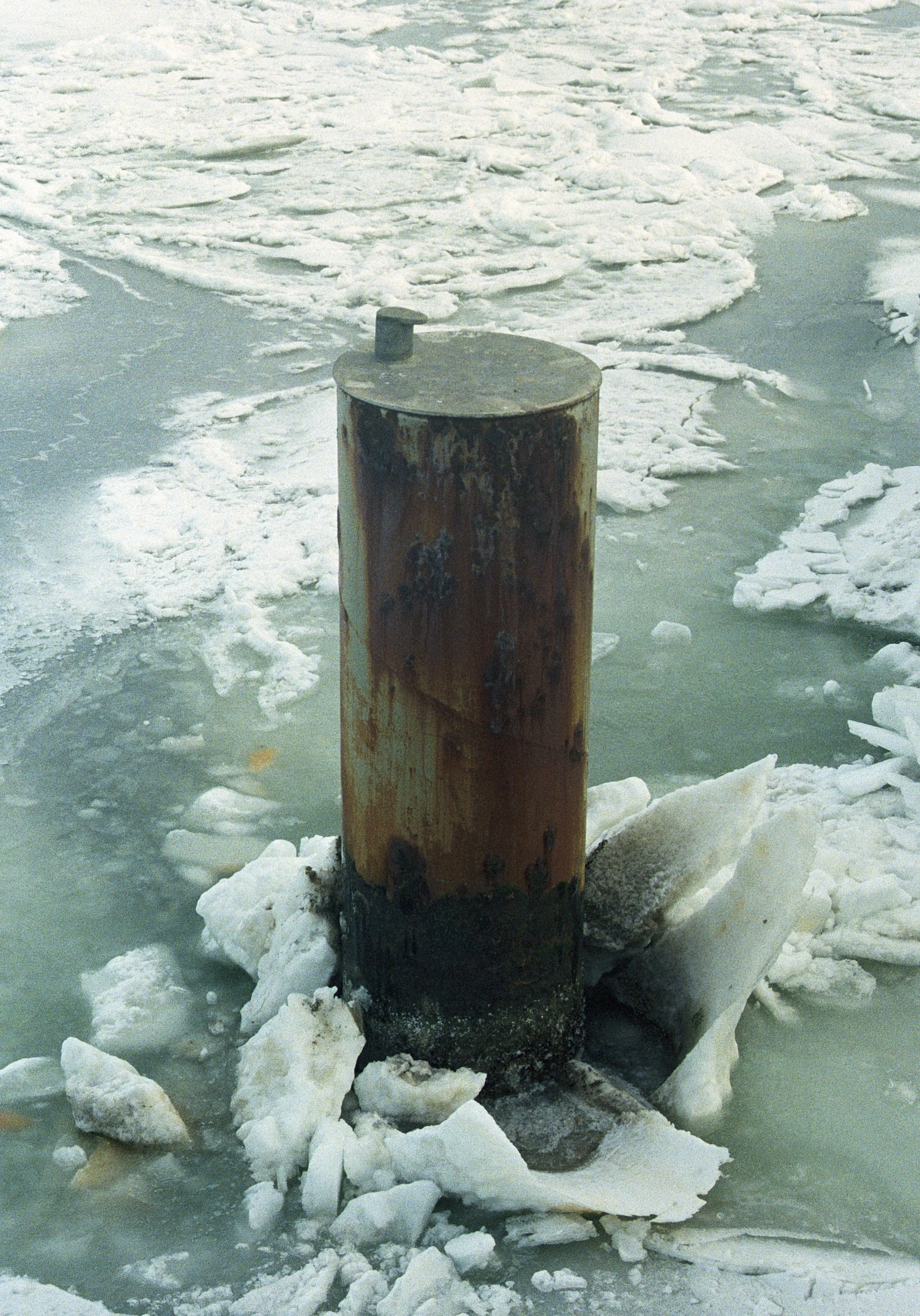 Ein rostiger Holzpfosten ragt aus gefrorenem Wasser und umgeben von Eisbrocken.