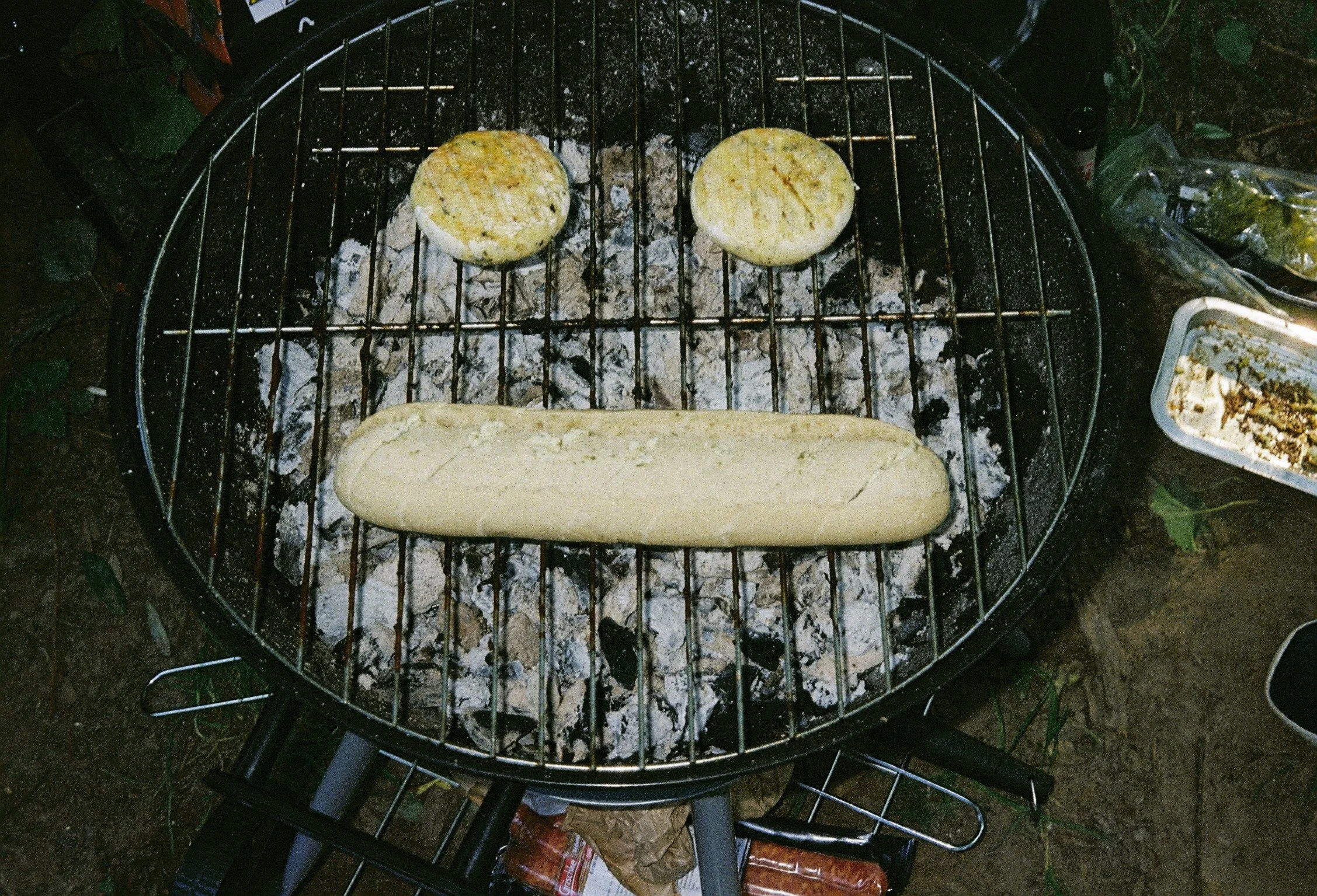Zwei Scheiben eines Brötchens oder Bagels werden auf einem Grill über Holzkohle gegrillt, mit Salz bestreut.