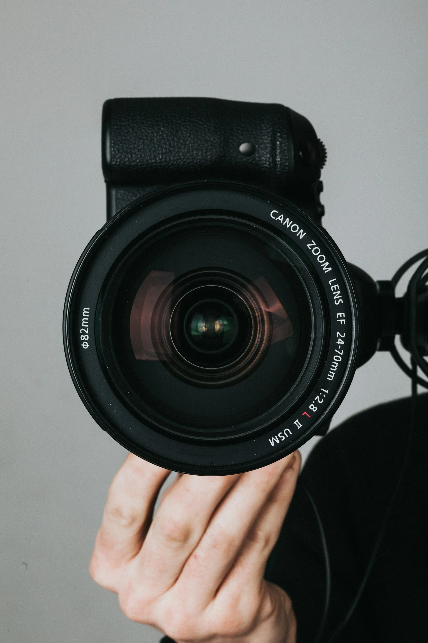 Person holding a professional camera with a large lens, on a gray background.