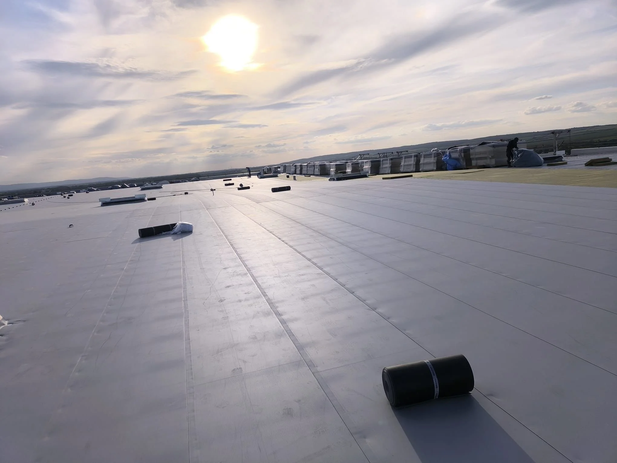 Rooftop mit Sonnenaufgang, mehrere schwarze Dämmstoffrollen und Arbeiter bei Dacharbeiten