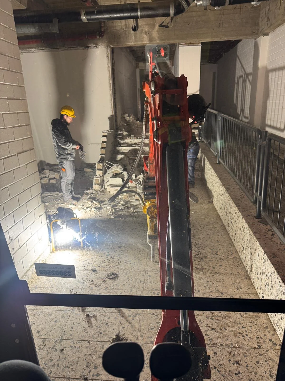 Bauarbeiter bei Abbrucharbeiten in einem Gebäude, mit Baumaschinen und Schutzhelmen, in einem Innenraum mit Fliesenboden.
