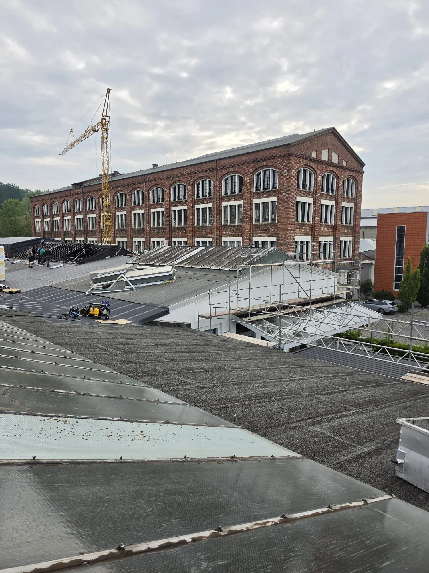 Mehrstöckiges Backsteingebäude unter Umbau mit Kran im Vordergrund und überwiegend bewölktem Himmel im Hintergrund.