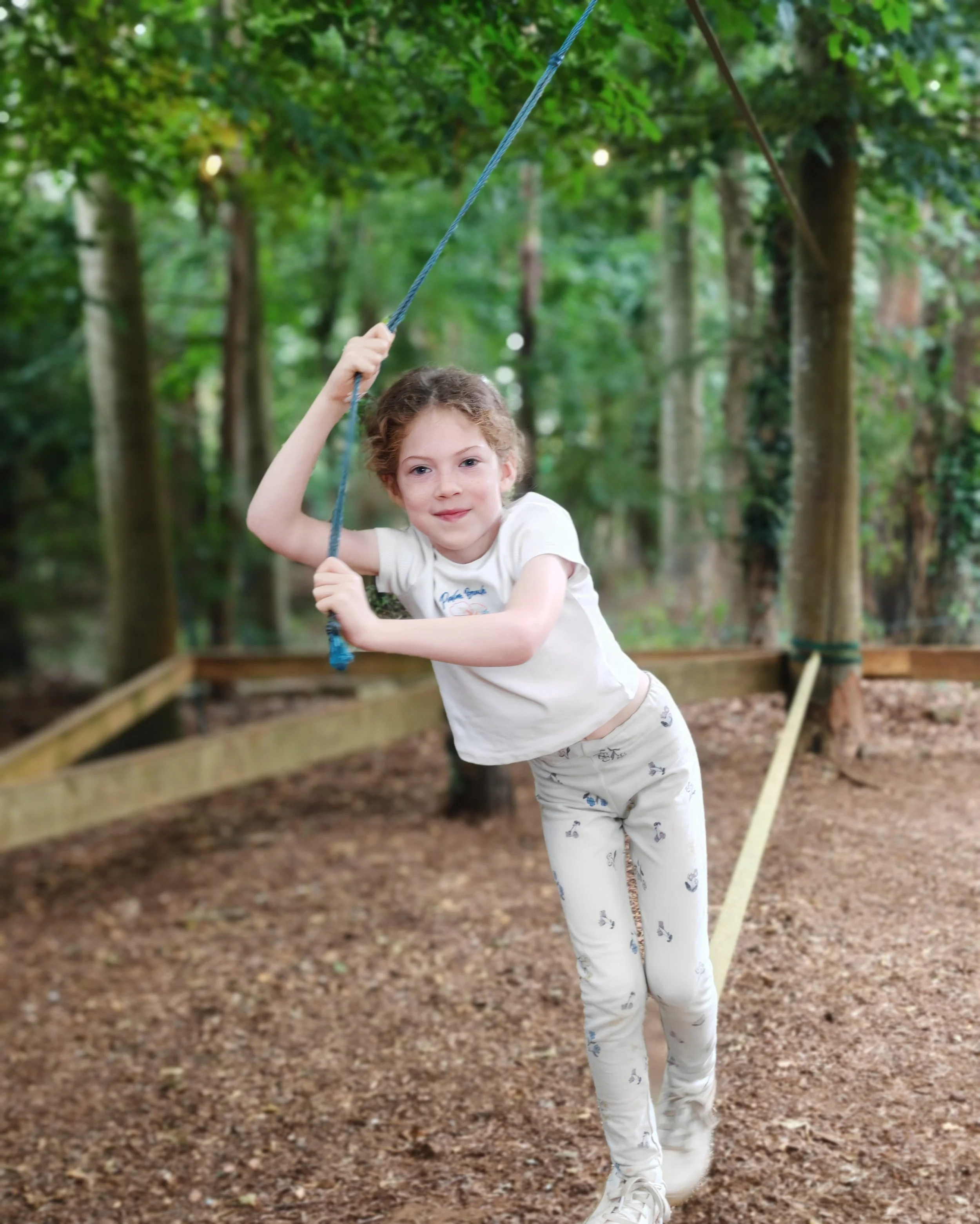 A white girl playing on a balancing beam supported by a blue rope at an activity centre