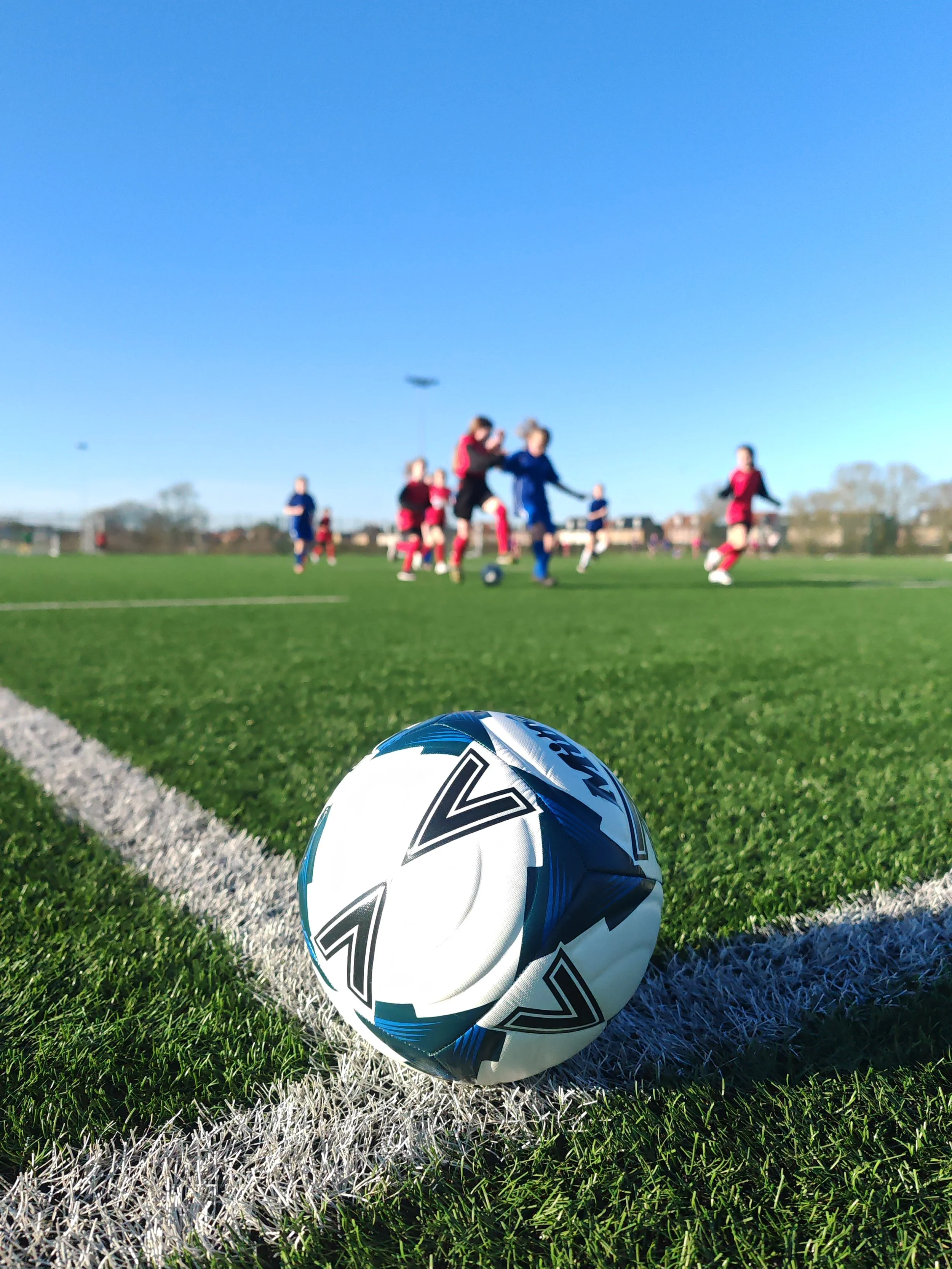 Girls football game with soft focus players in distance with black and white football in the foreground
