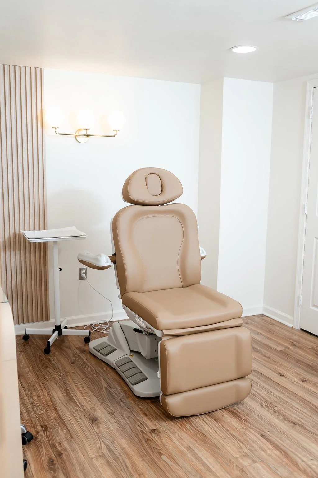 Medical examination chair in a clean, well-lit clinic room with wooden flooring and minimalist decor.