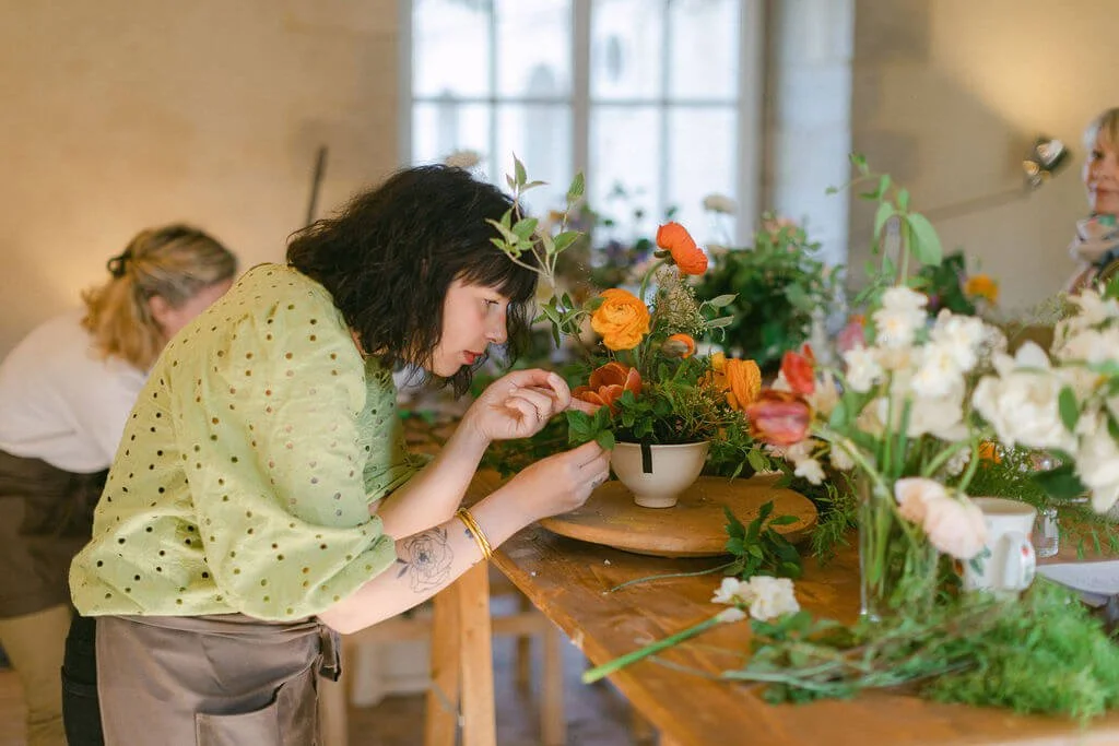 Participante en train de composer avec des fleurs de saison pendant l’Atelier Devenir Fleuriste.