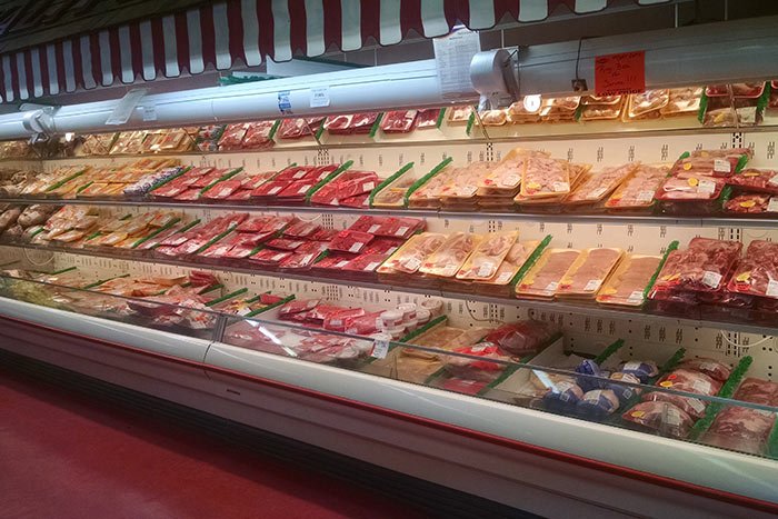 A meat display case in a grocery store with various packaged meats on multiple shelves.