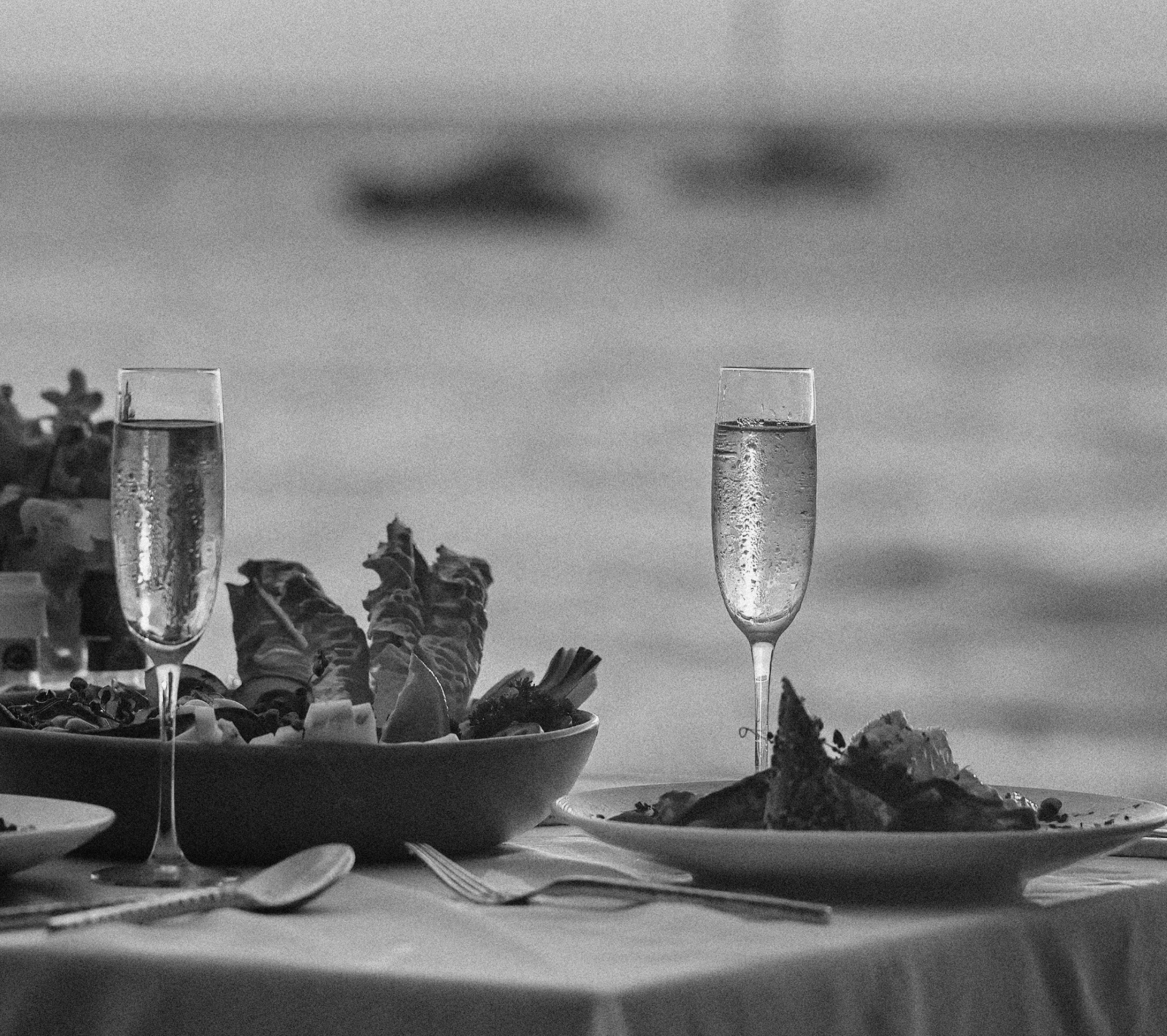 Two champagne glasses filled with bubbly, set on a table with a large bowl of snacks, with a scenic outdoor view in the background.