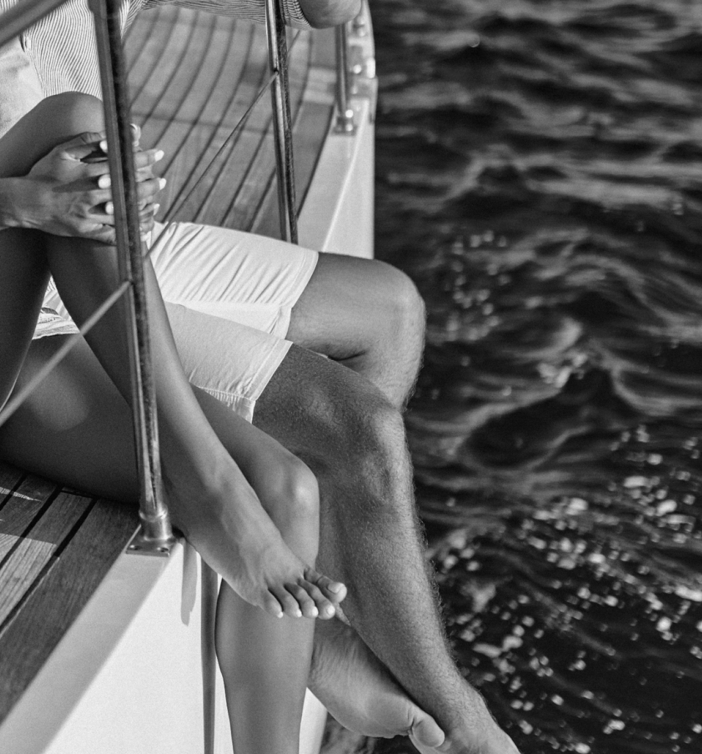 A person sitting on the edge of a boat, with legs hanging over the side, touching the water below.