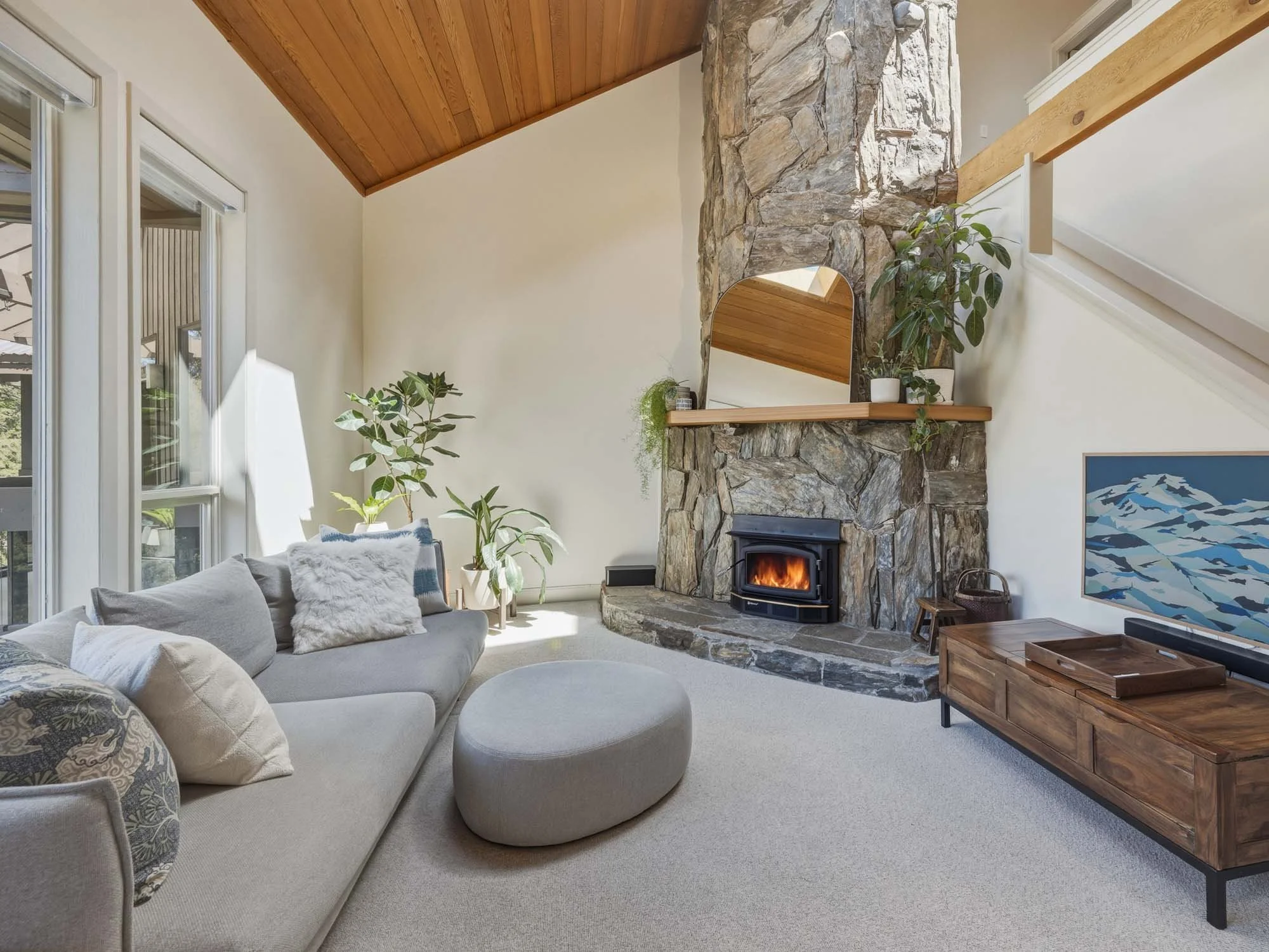 The open-concept, thoughtfully designed family room at 205-6117 Eagle Drive, showing a spacious sectional sofa anchored by the feature stone wood-burning fireplace and automated window treatments.