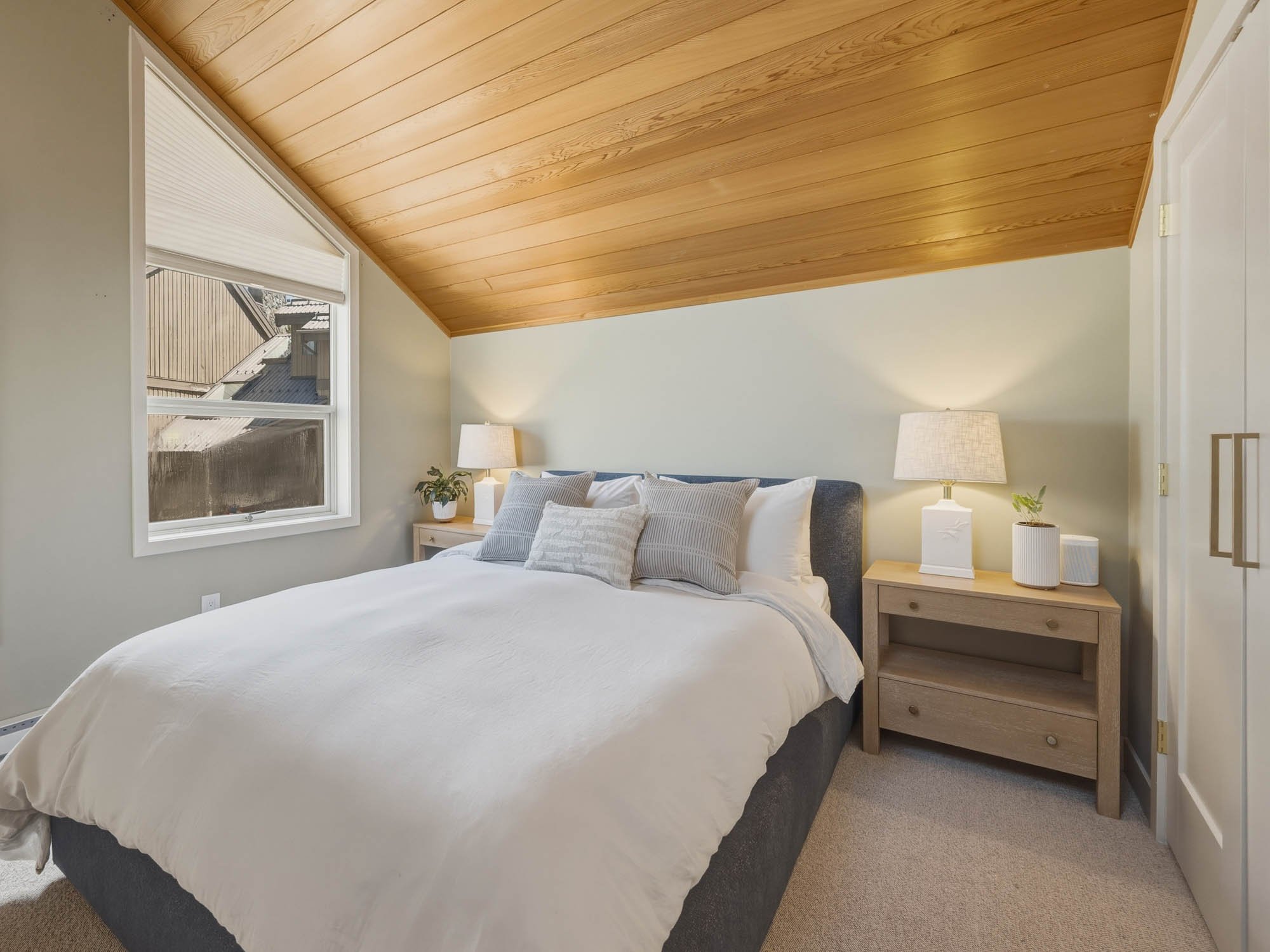 Private upper-level master bedroom retreat within this Whistler 2-bedroom townhouse for sale, featuring cozy alpine design, a sloped wood ceiling, and window treatments with Ryse automated controls.