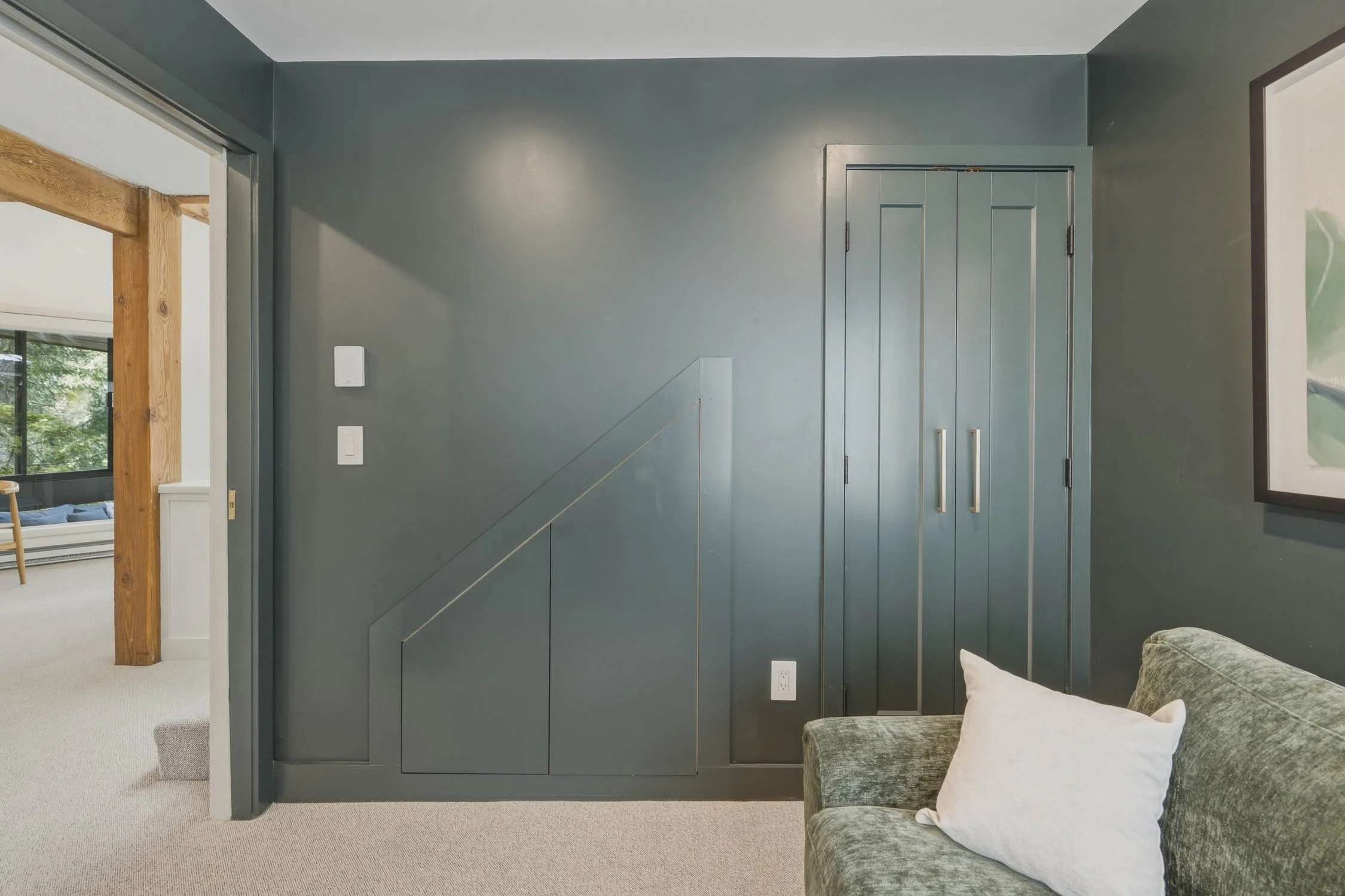 Interior view of a room with a dark green built-in wardrobe, a grey wall, and a cozy green armchair with pillows.