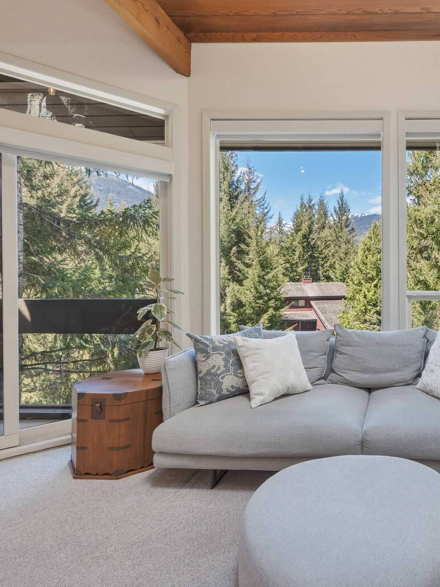 Bright open living area in this Whistler 2-bedroom townhouse for sale, highlighting large scenic windows with alpine mountain views and custom automated Hunter Douglas blinds.