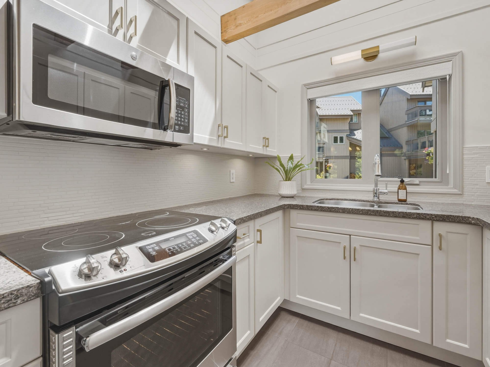 High-end cooking station in the kitchen of 205-6117 Eagle Drive, featuring a built-in microwave, drop-in stovetop, premium stone counters, and a high-performing Bosch dishwasher nearby.
