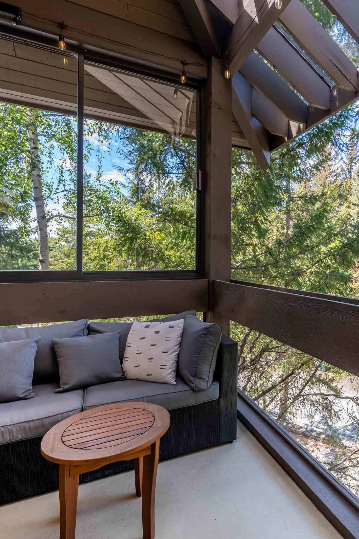 Private outdoor living space at the Sunrise Whistler Cay Heights townhome, highlighting an expansive covered balcony with comfortable patio seating overlooking mature evergreen trees.