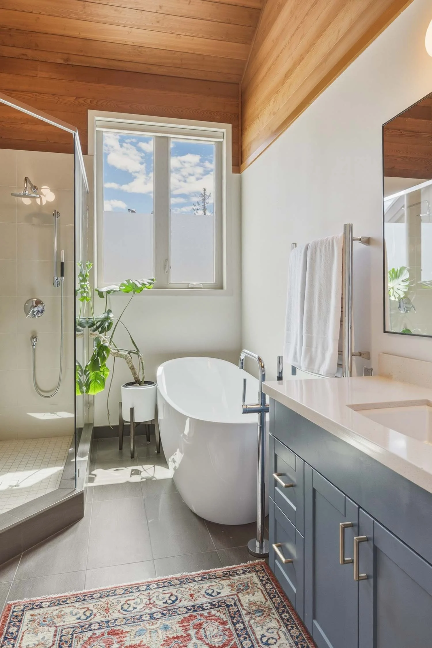 Large 3-piece primary ensuite bathroom at 6117 Eagle Drive featuring programmable heated tile floors, a custom double vanity, a glass shower enclosure, and a programmable heated towel warmer.