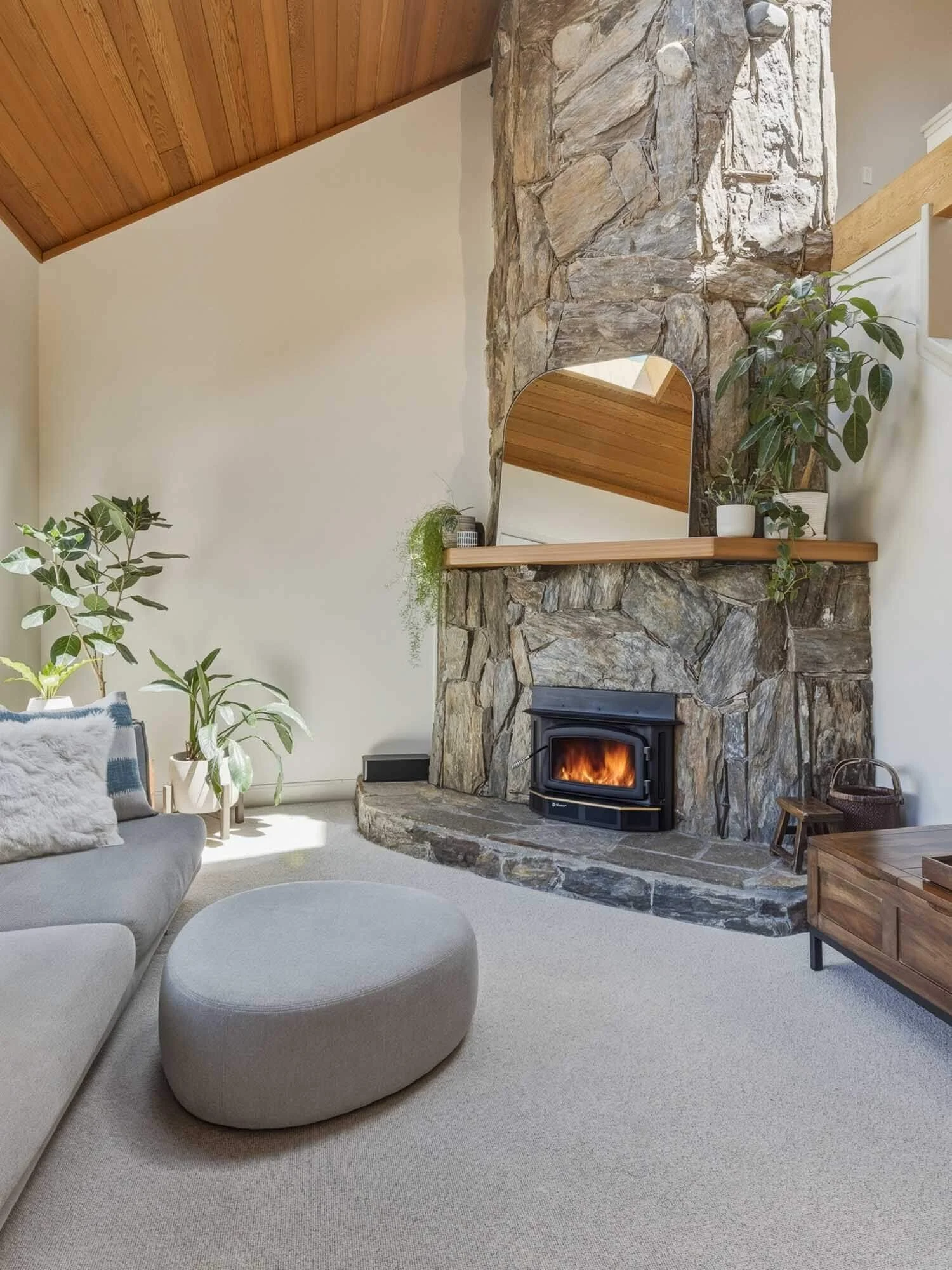 Cozy main living room layout at 205-6117 Eagle Drive showcasing a feature stone wall with a premium Regency wood-burning fireplace, vaulted wood ceilings, and comfortable modern seating.