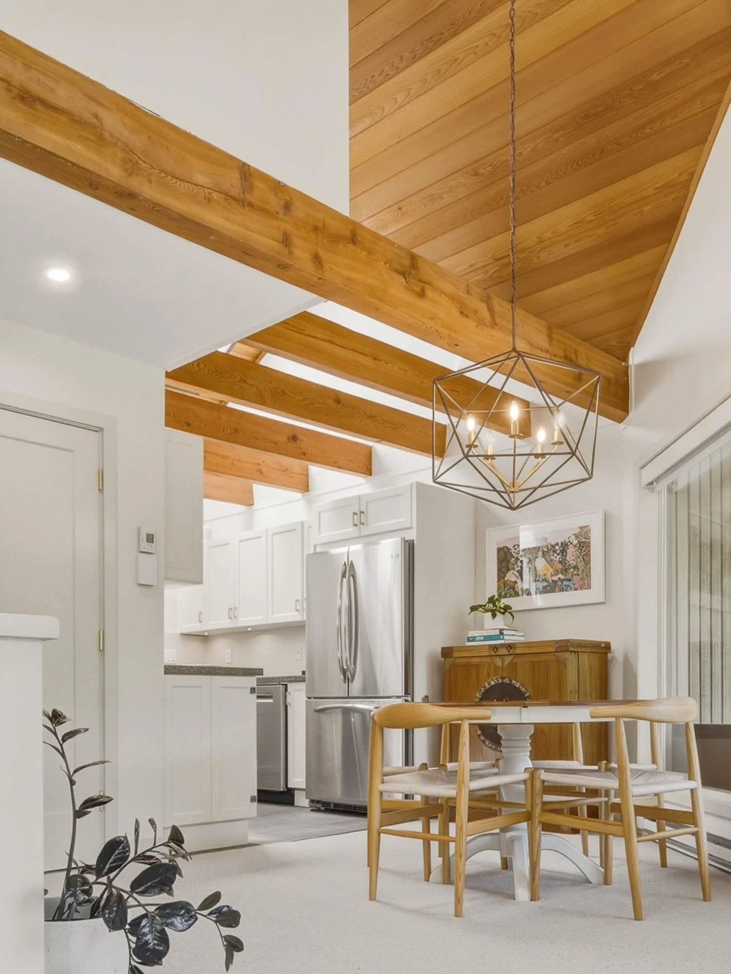 Light-filled kitchen and dining room layout inside this Whistler 2-bedroom townhouse for sale, highlighting the dramatic vaulted natural wood ceilings, structural beams, and a modern geometric chandelier.