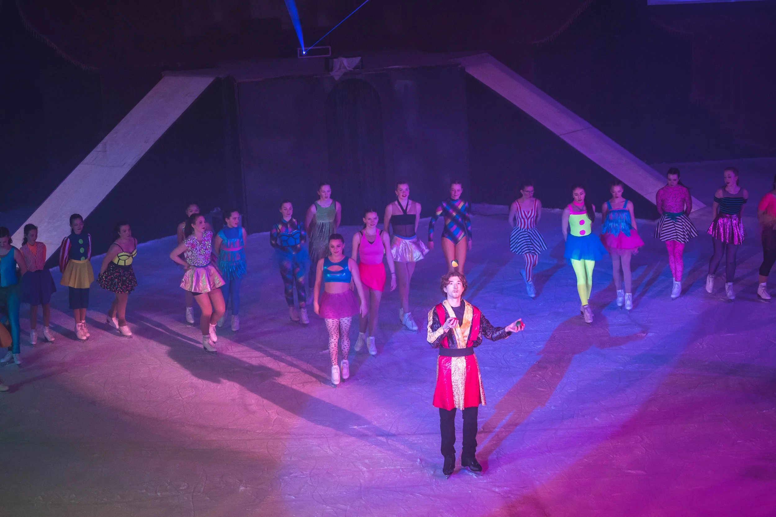 A group of performers dressed in colorful costumes are walking on stage during a show, with some people holding hands and others walking with confident expressions.